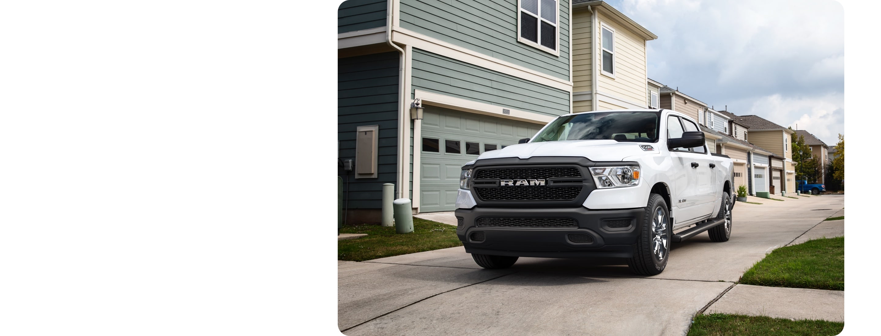 Vista frontal de medio perfil de una Ram 1500 Tradesman HFE EcoDiesel 2021 blanca estacionada detrás de una fila de casas.