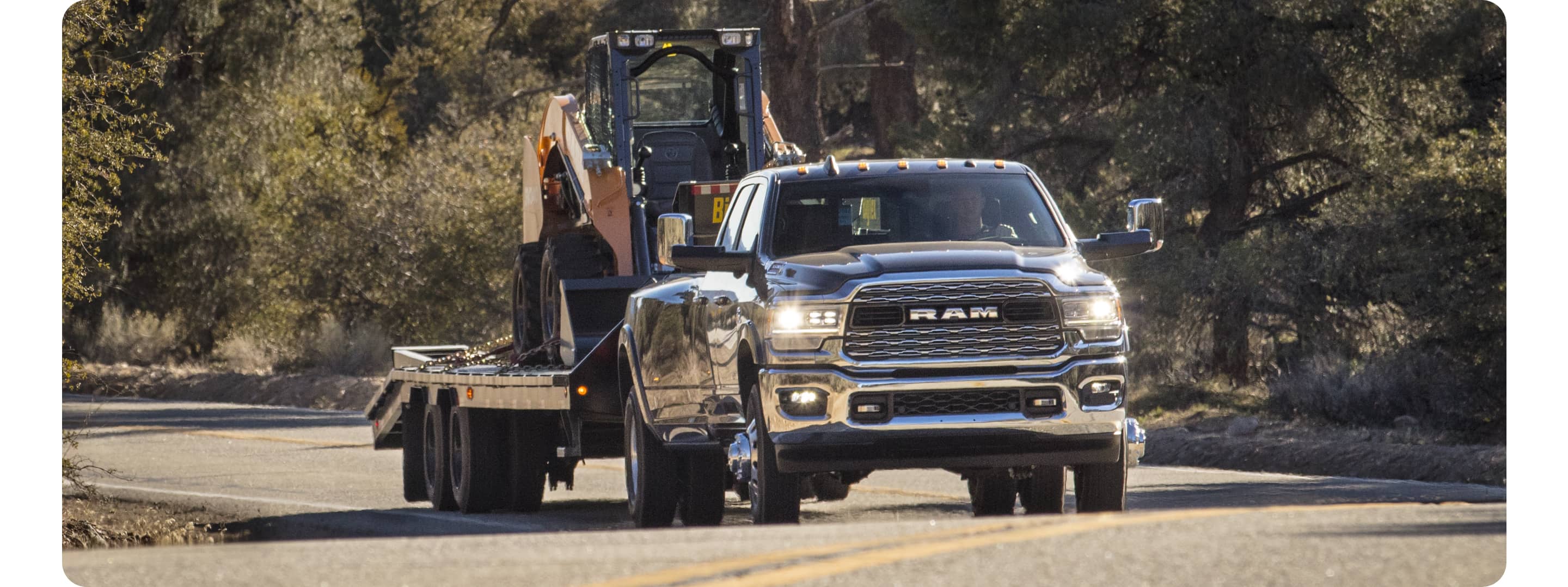 Una Ram 3500 Limited 2021 andando por una carretera, remolcando equipo de construcción pesado en un tráiler.