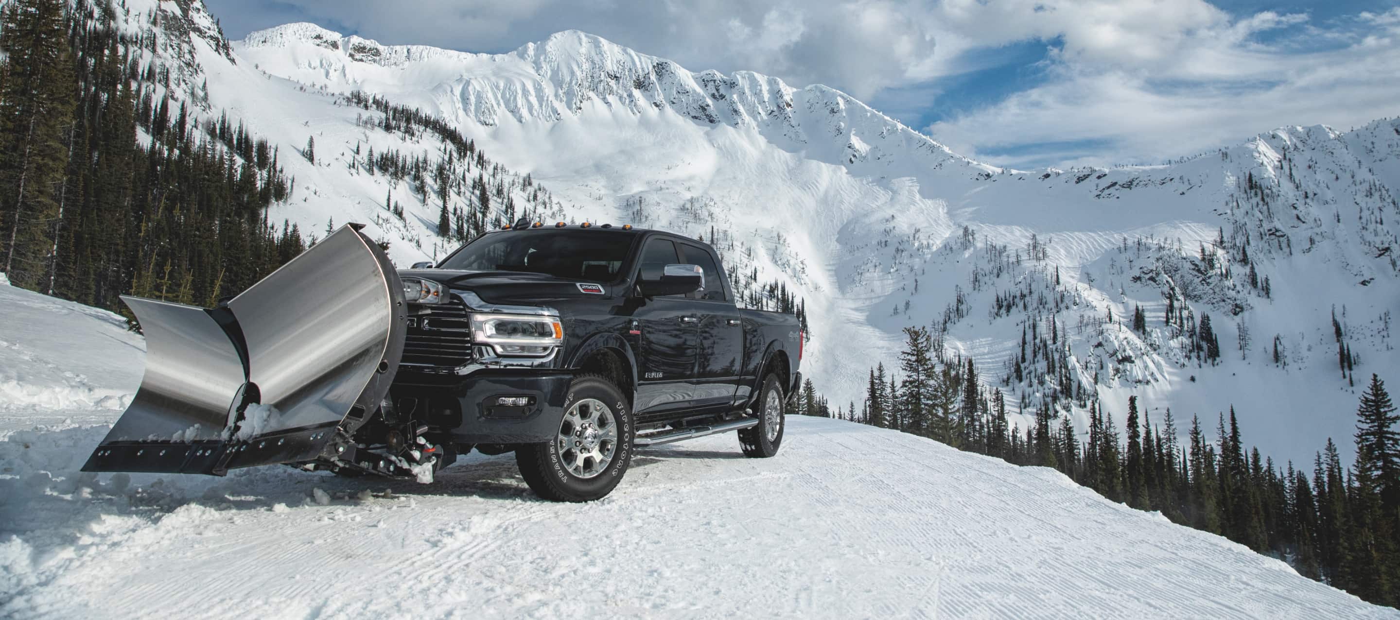 Una Ram 2500 Laramie 4x4 2022 con una pala en v de acero inoxidable, despejando nieve en la cumbre de una colina en las montañas.