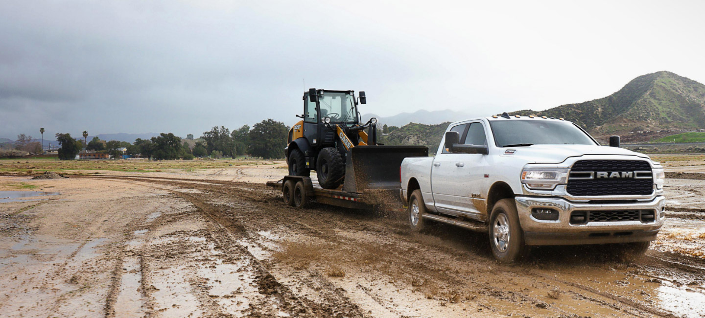 Una Ram 2500 Big Horn 4x4 Crew Cab 2022 remolcando una excavadora por un campo embarrado.
