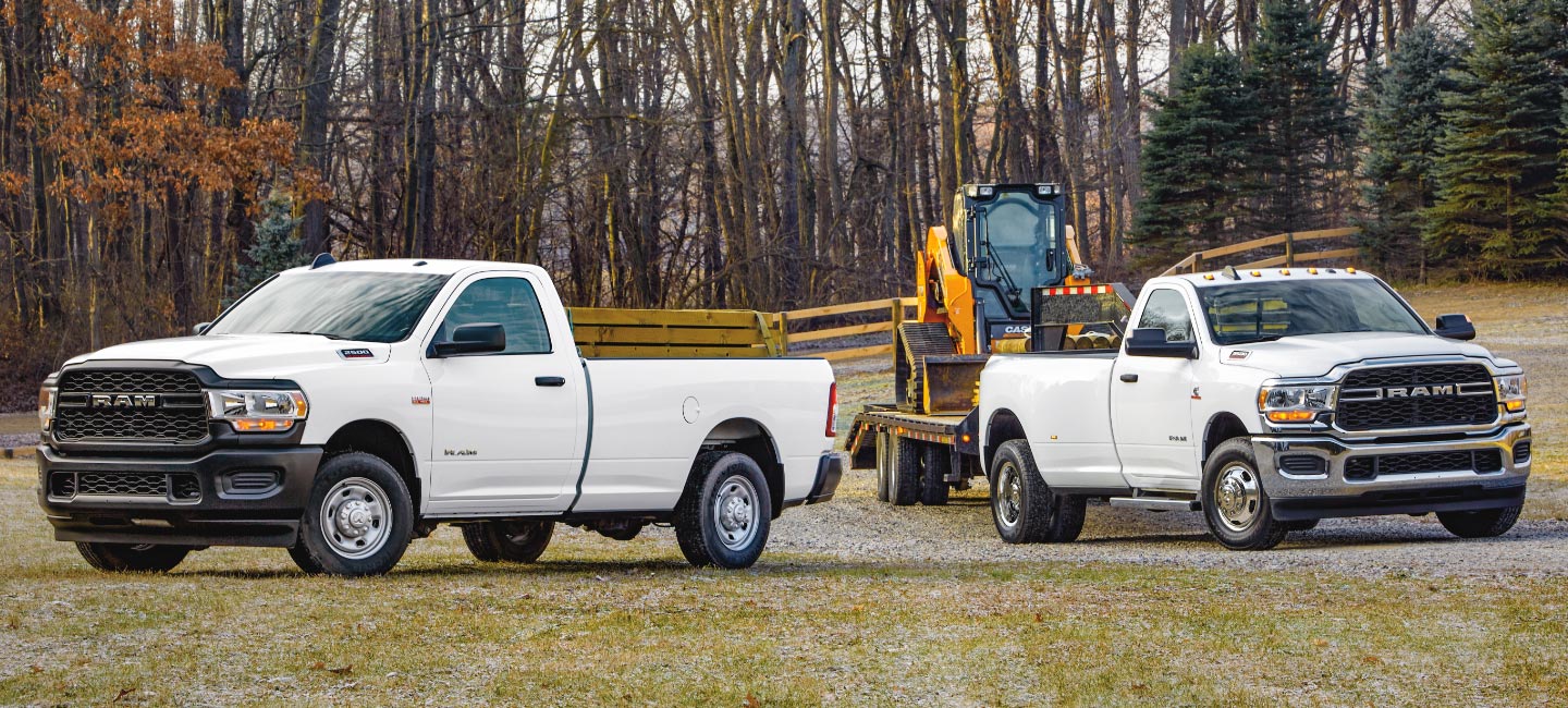 Una Ram 2500 Tradesman 4x4 Regular Cab 2022 y una Ram 3500 Tradesman 4x4 Regular Cab 2022 estacionadas de modo de formar un ángulo recto entre sí, en un claro en el bosque. La 3500 remolcando una excavadora.