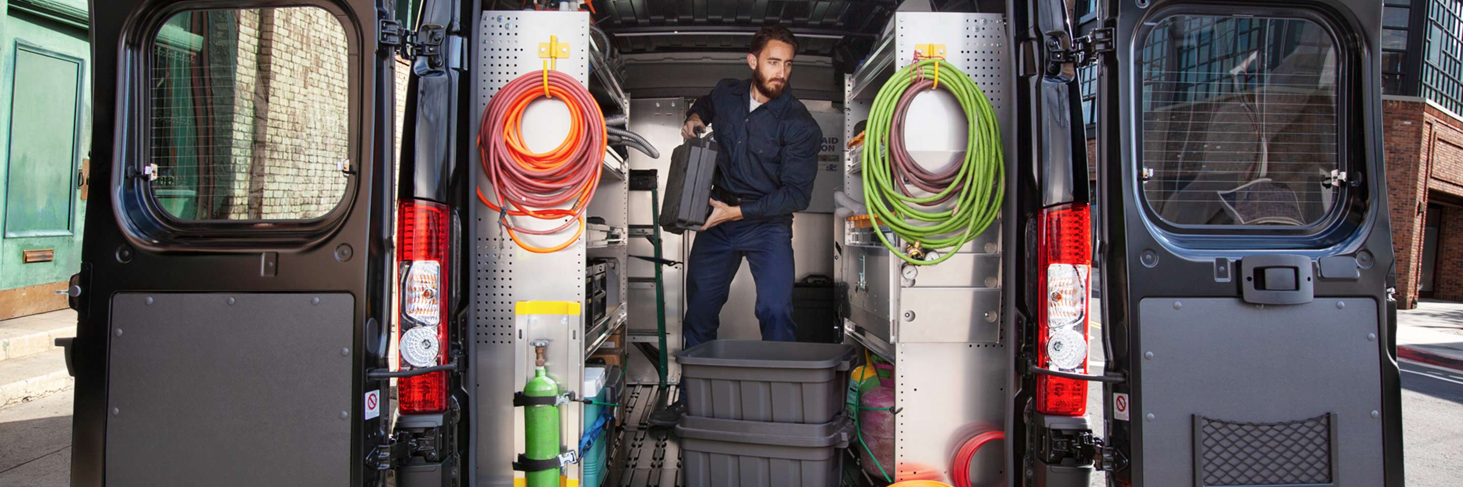 Una Ram ProMaster 2022 con su compartimento de carga equipado con estantes. Un hombre de pie dentro de la van.