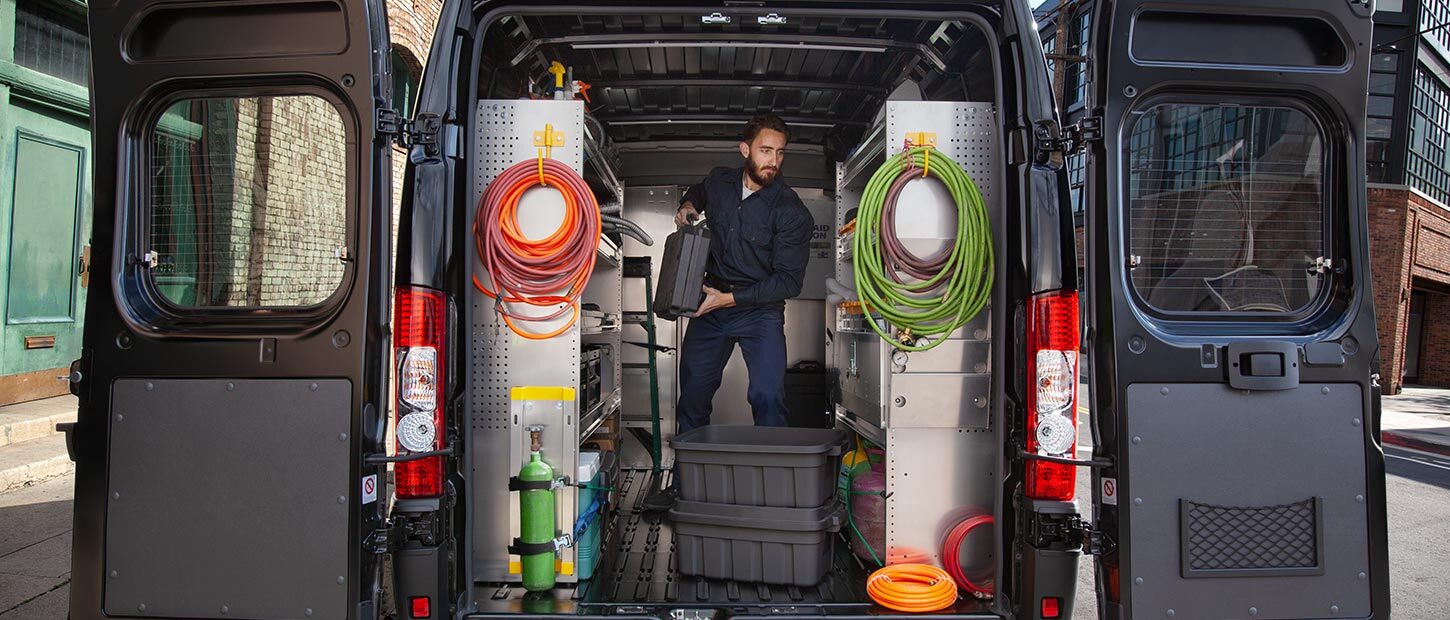 Una Ram ProMaster 2022 con su compartimento de carga equipado con estantes y ganchos para cables. Un hombre de pie dentro de la van.