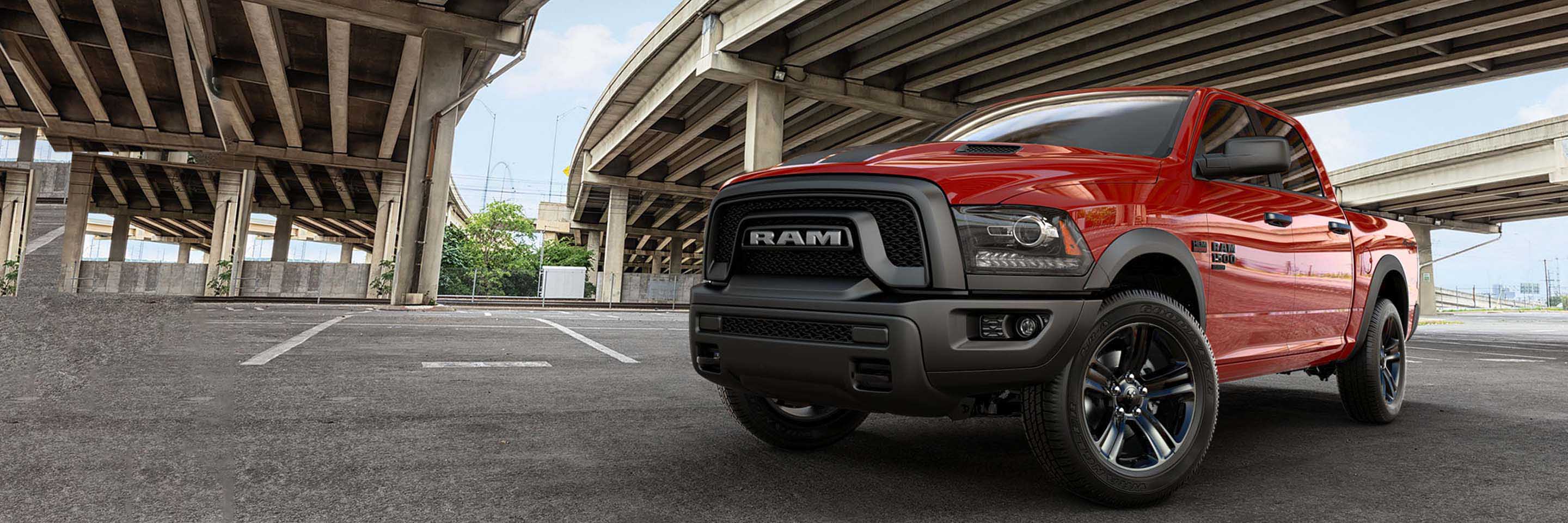 Una Ram 1500 Classic Warlock Crew Cab 2023 4x4 roja estacionada debajo de un paso elevado de autopista.