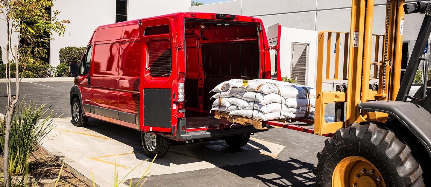Un montacargas cargando un palé apilado con sacos a través de las puertas traseras de la Cargo Van Ram ProMaster 2500 2023.