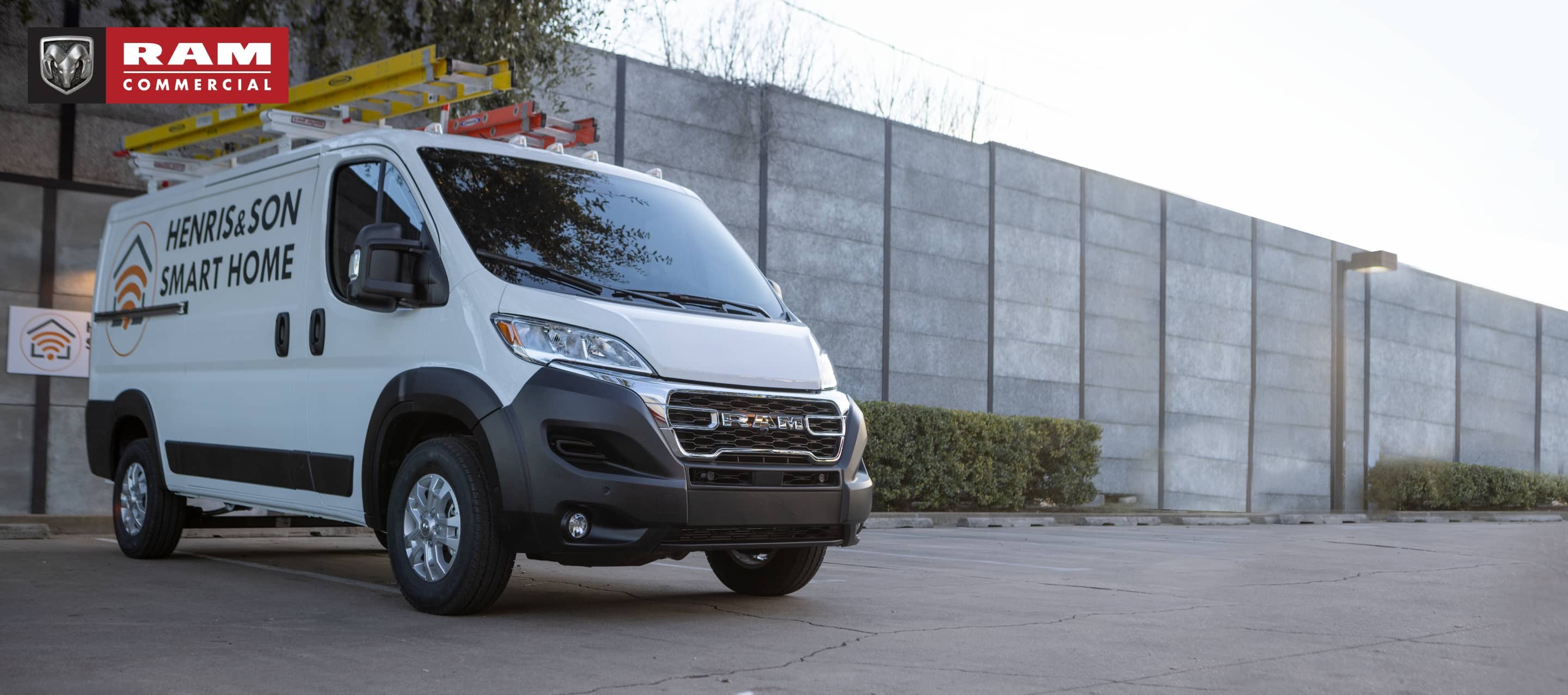 Una Ram ProMaster 1500 Low Roof Cargo Van 2023 con gráficas de una empresa de seguridad en su costado, estacionada al lado de un edificio comercial. Publicidad de Ram.