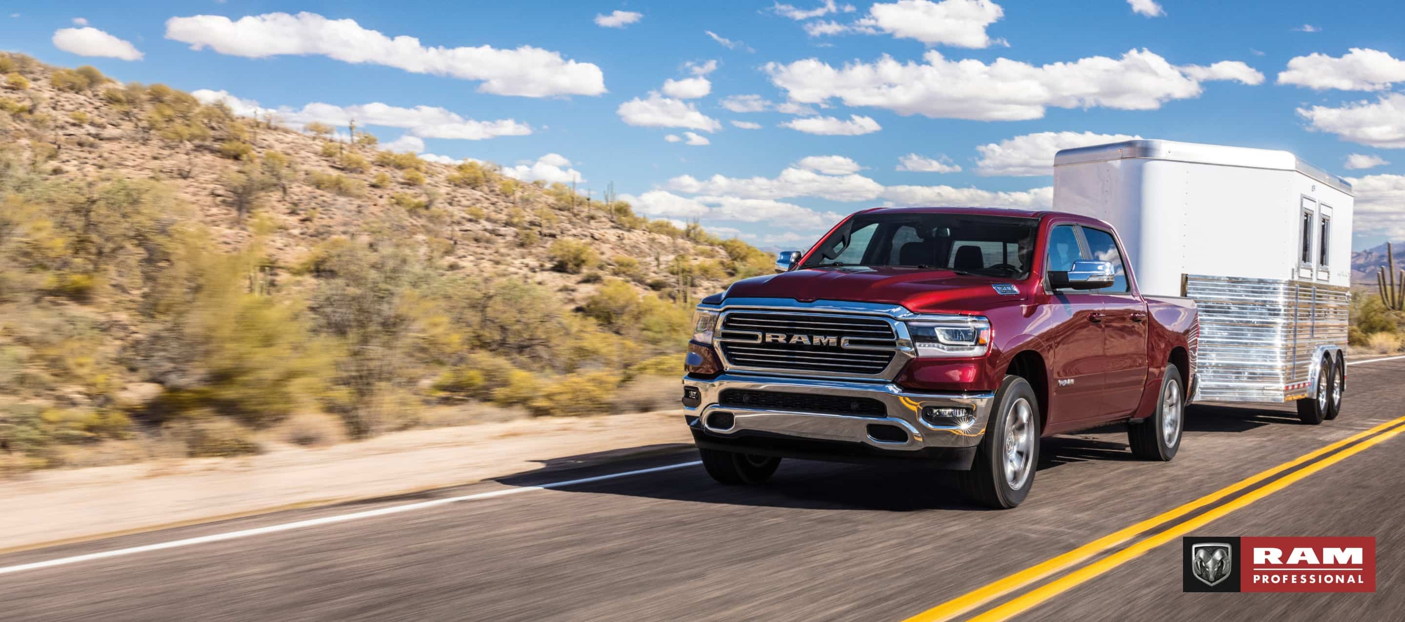 Una Ram 1500 Laramie Crew Cab 2024 roja remolcando un remolque de caballo mientras circula por una carretera en el desierto. Ram Professional.