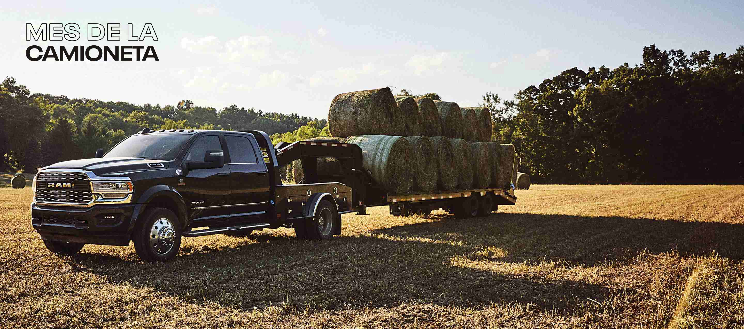 Una Ram 5500 Limited 4x4 Chassis Crew Cab 2024 negra con un remolque de cuello de cisne cargado con varios fardos de heno, estacionado en un campo abierto. Mes de las camionetas.