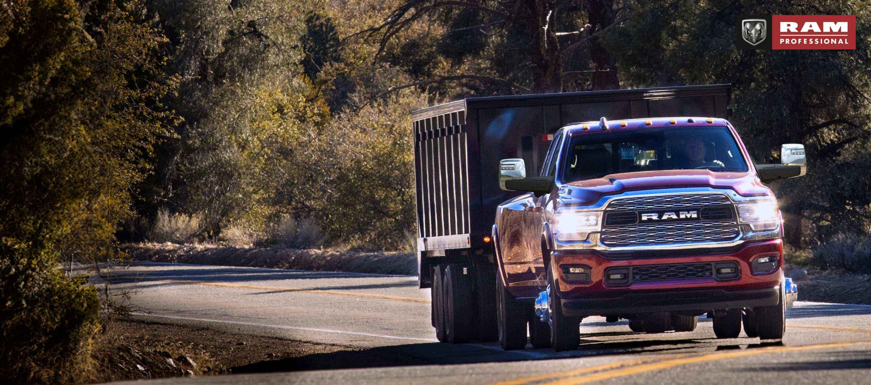 Una Ram 3500 4x4 Crew Cab 2024 roja circulando por una carretera en el bosque, acarreando un remolque de carrocería volcadora. Ram Professional.