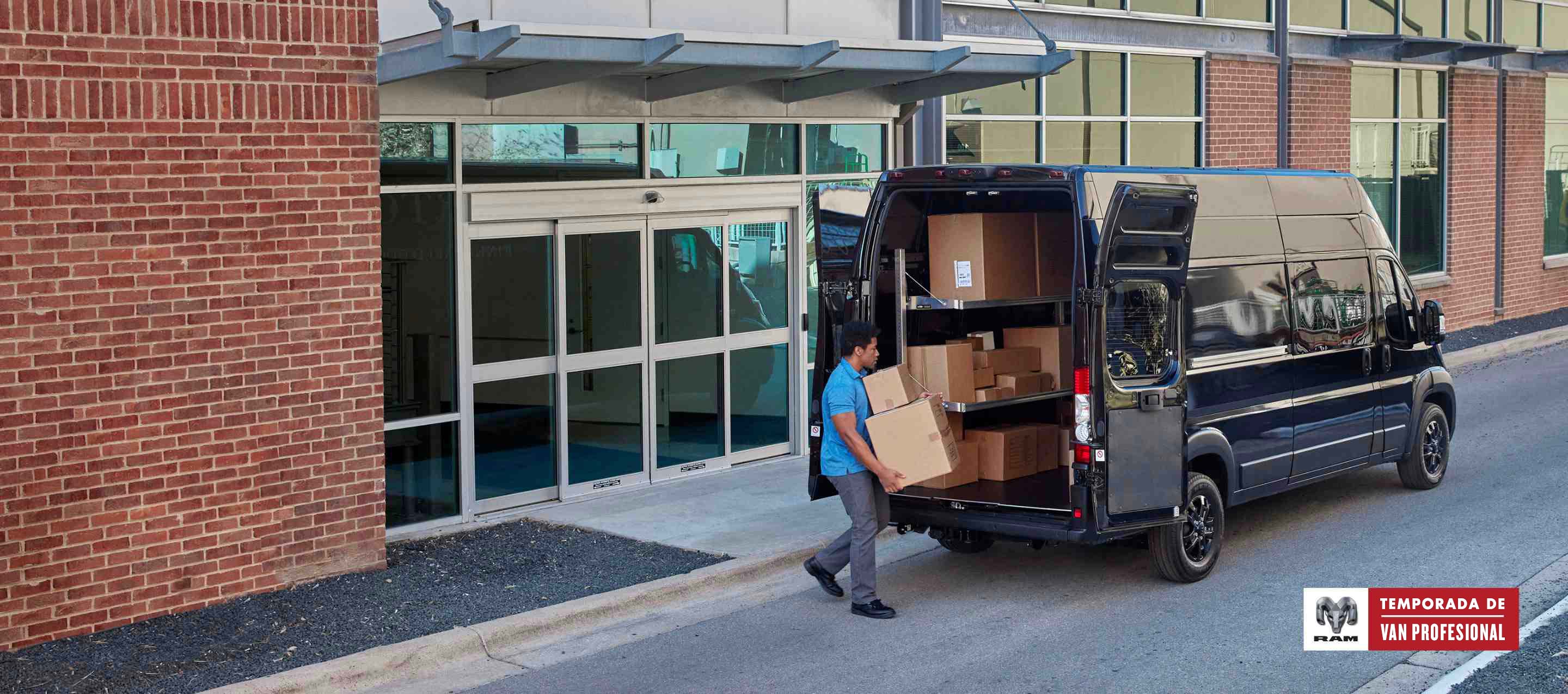 Un hombre con cajas acercándose a las puertas traseras abiertas de una Ram ProMaster 3500 SLT Plus Cargo Van Super High Roof 2024 negra con el paquete de apariencia en negro. Temporada de vans profesionales.