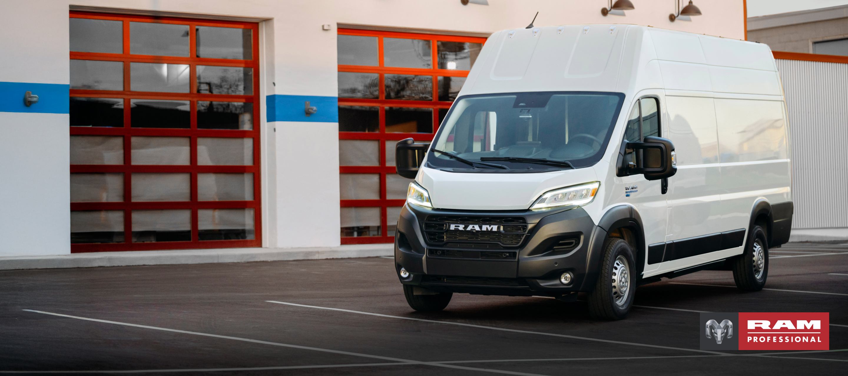 Ángulo delantero del lado del pasajero de una van Ram ProMaster EV 3500 Super High Roof Step 2024 blanca estacionada cerca de un garaje comercial. Ram Professional.