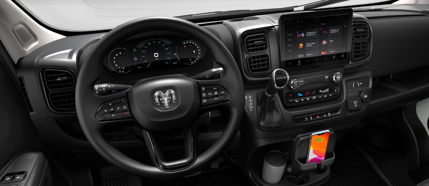 El volante, la pantalla digital de información para el conductor en el panel de instrumentos, la pantalla táctil Uconnect, los controles de la consola central y la base de carga inalámbrica en la Ram ProMaster 2024.