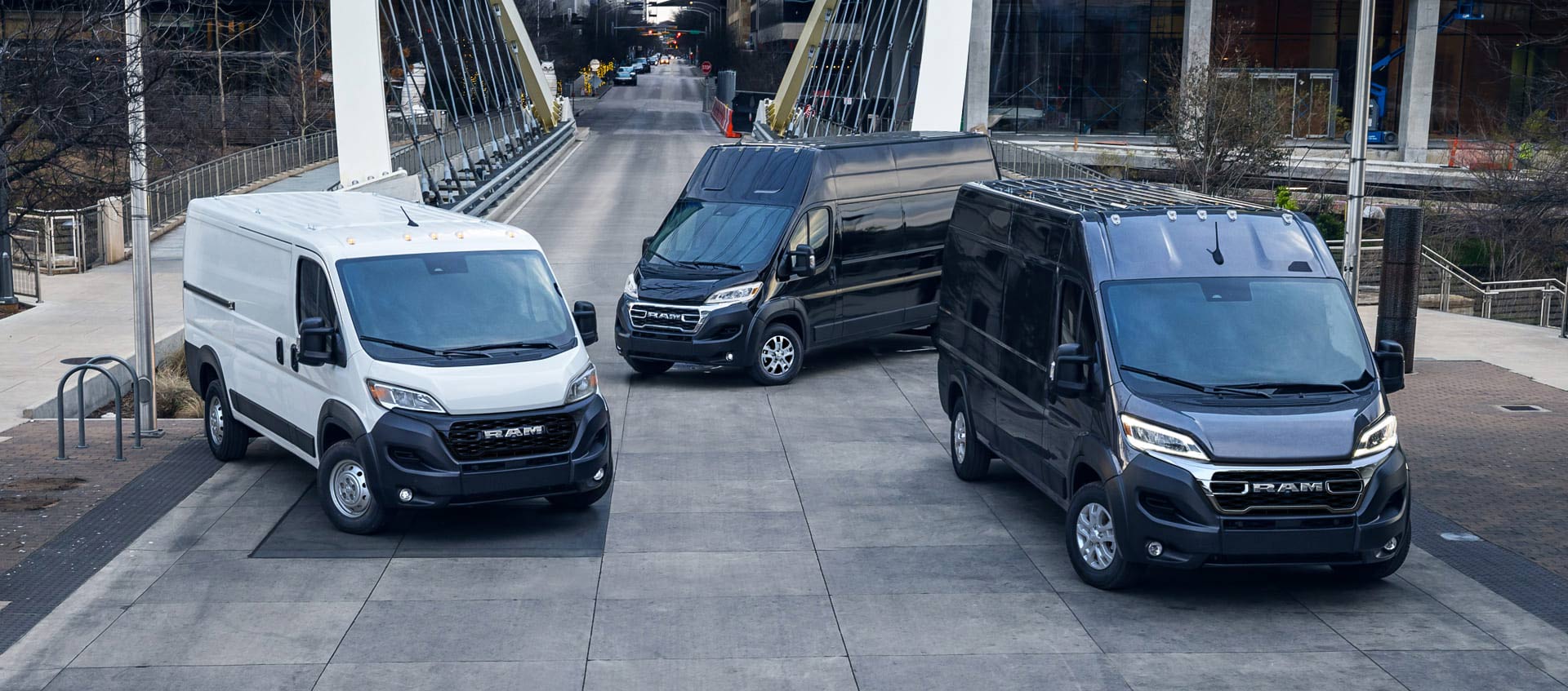 Tres vans de carga Ram ProMaster 2025. De izquierda a derecha: una Ram ProMaster Tradesman Standard Roof 1500 blanca, una SLT Plus Super High Roof 3500 negra y una SLT High Roof 3500 negra.