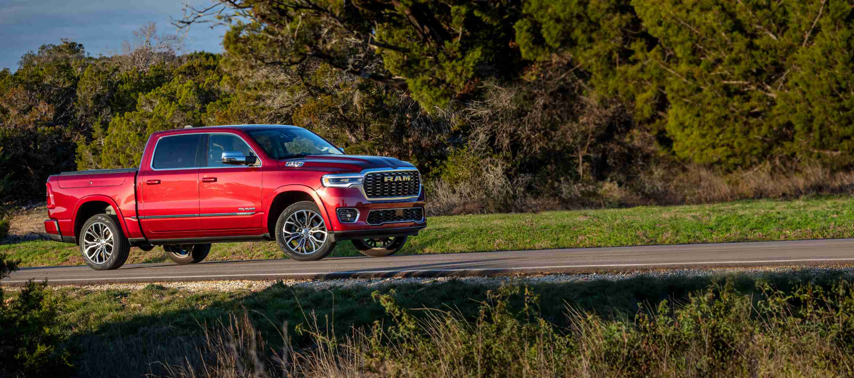 Perfil del lado del pasajero de la Ram 1500 Tungsten Crew Cab 2025 roja estacionada al costado de un camino rural.