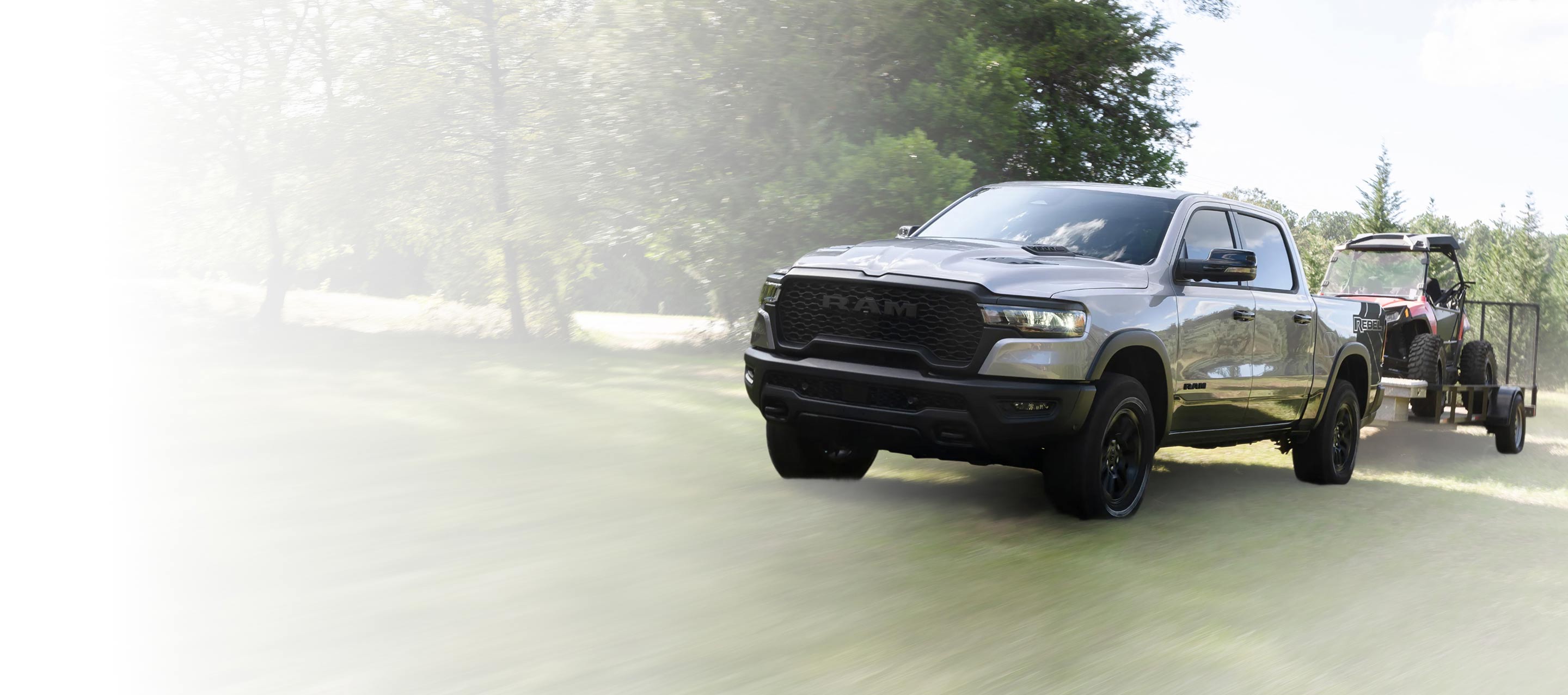 Una Ram 1500 Rebel 4x4 Crew Cab 2025 gris remolcando un ATV sobre un remolque utilitario.