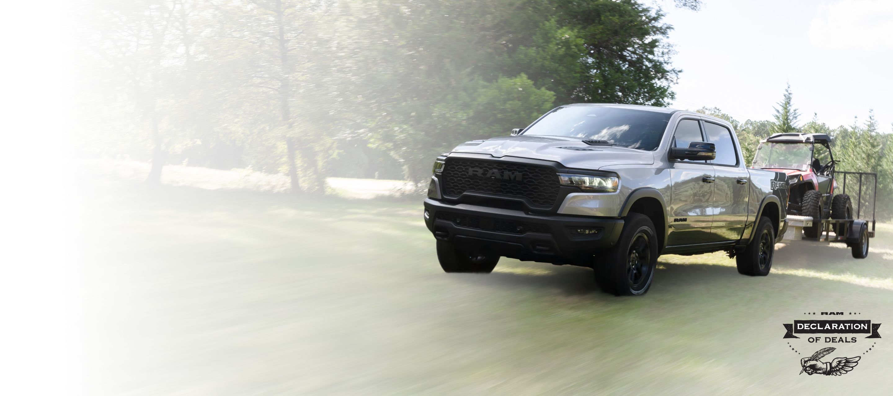 Una Ram 1500 Rebel 4x4 Crew Cab 2025 gris remolcando un ATV sobre un remolque utilitario. Evento de ventas Declaración de ofertas.