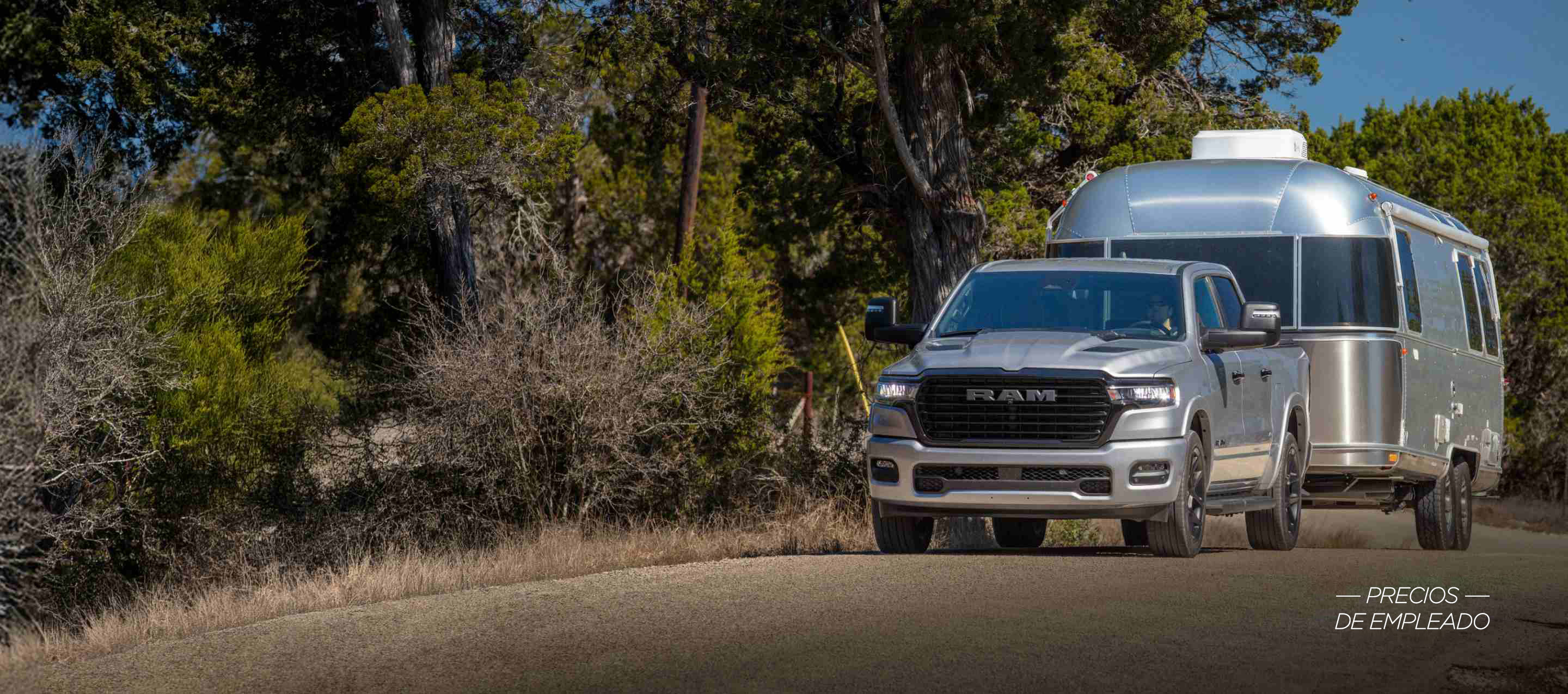 Una Ram 1500 Tungsten Crew Cab 2025 plateada circulando por un puente de una autopista en una ciudad con edificios altos de fondo. Employee Pricing Plus Sales Event.