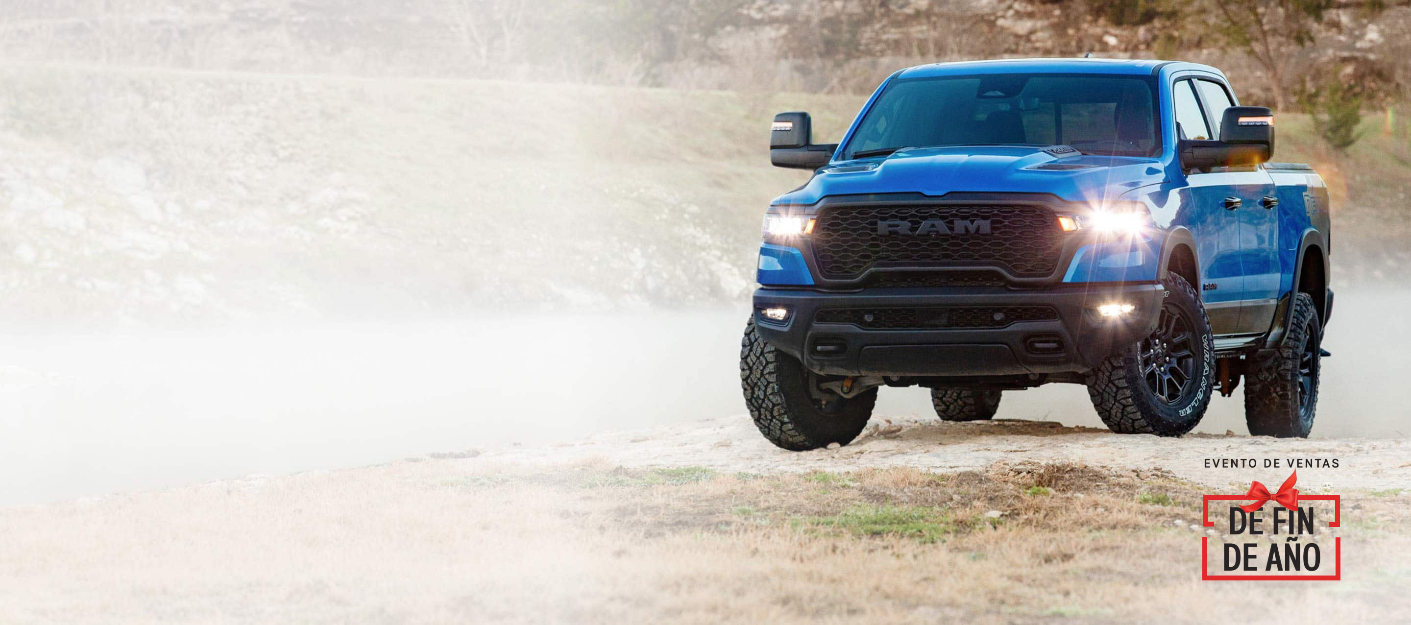 Una Ram 1500 Rebel 4x4 Crew Cab 2025 azul, con sus faros delanteros y antiniebla encendidos, sube una pequeña colina fuera de la carretera. Evento de ventas de Fin de año.