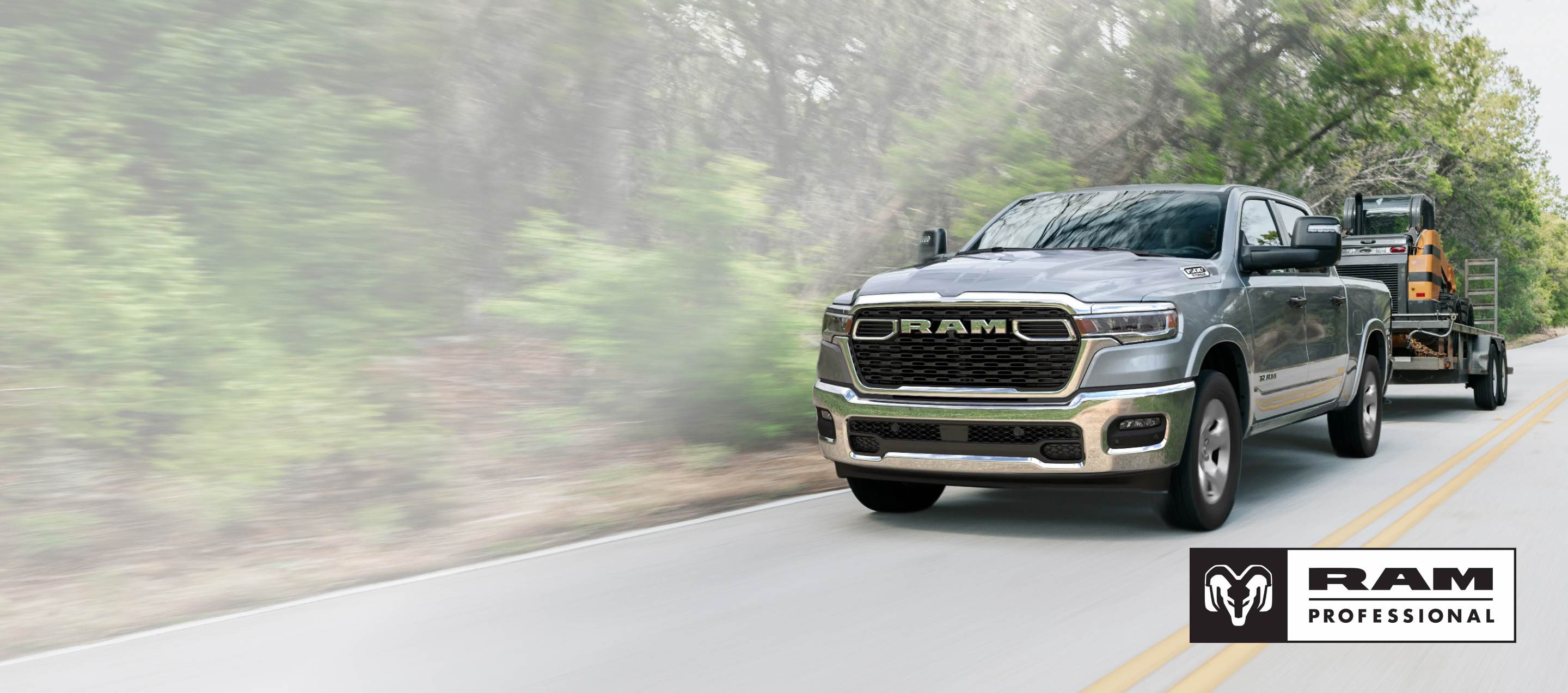 Una Ram 1500 Big Horn 4x4 Crew Cab 2025 plateada remolcando equipos motorizados mientras viaja por una carretera. Ram Professional.