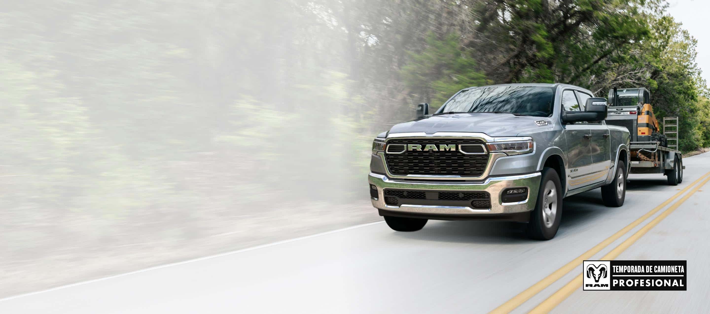 Una Ram 1500 Big Horn 4x4 Crew Cab 2025 plateada remolcando equipos motorizados mientras viaja por una carretera. Temporada de camionetas Ram Professional.