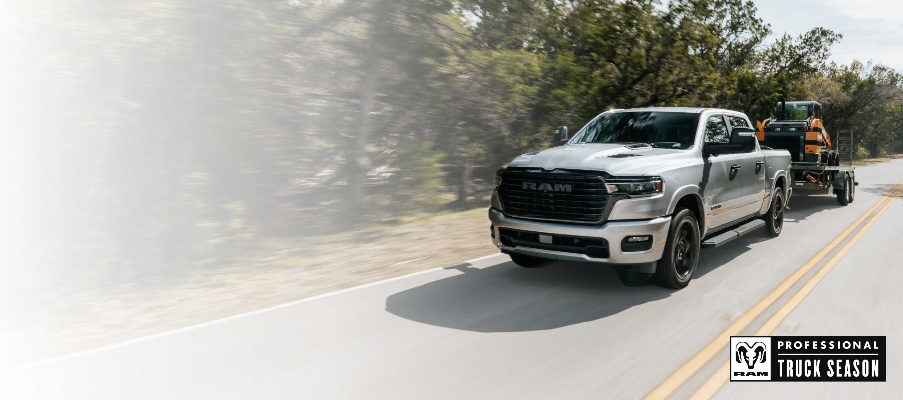 Una Ram 1500 Laramie 4x4 Crew Cab 2025 plateada circulando por una autopista y remolcando un vehículo de construcción en un remolque basculante. Temporada de camionetas Ram Professional.