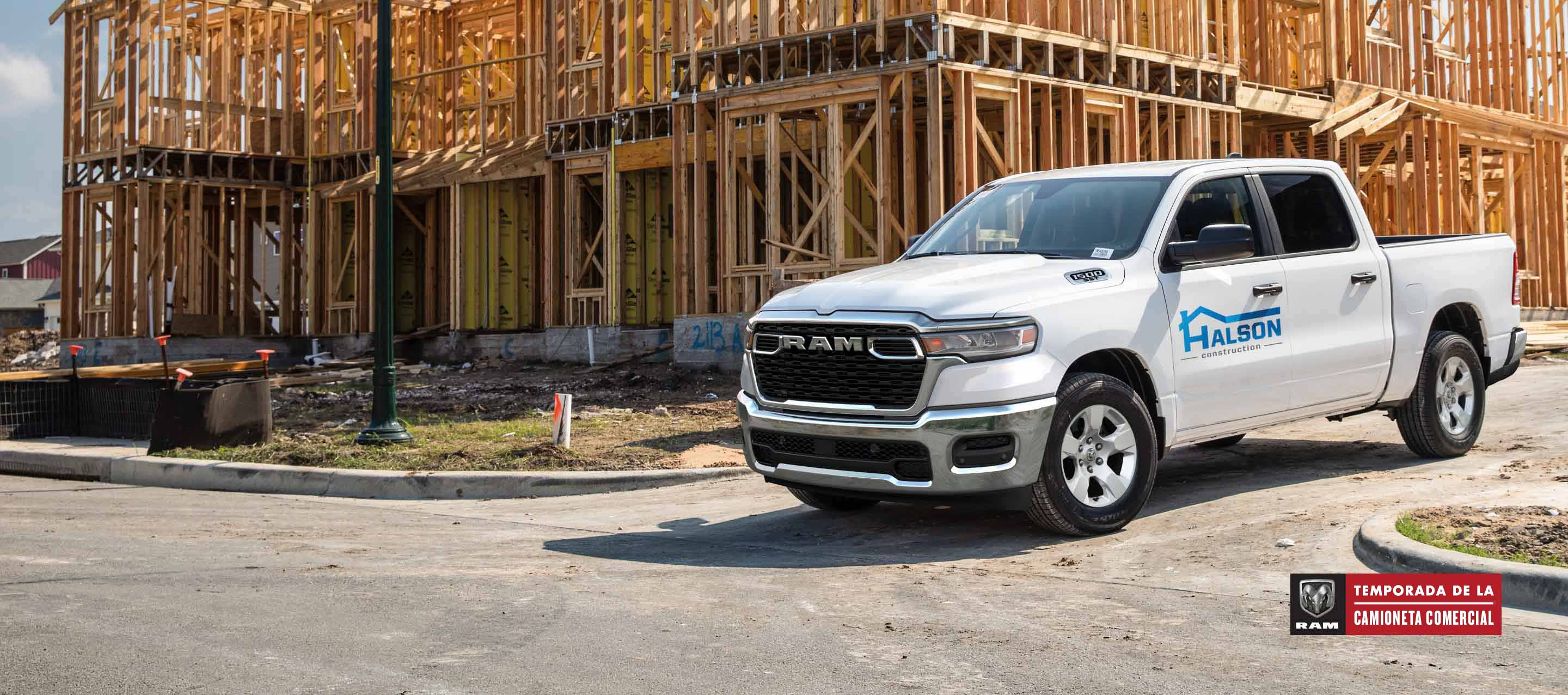 Una Ram 1500 Tradesman 4x4 Crew Cab 2025 blanca, con gráfico de una compañía de construcción en la puerta del conductor, saliendo de una obra de construcción comercial. Temporada de la camioneta comercial Ram.