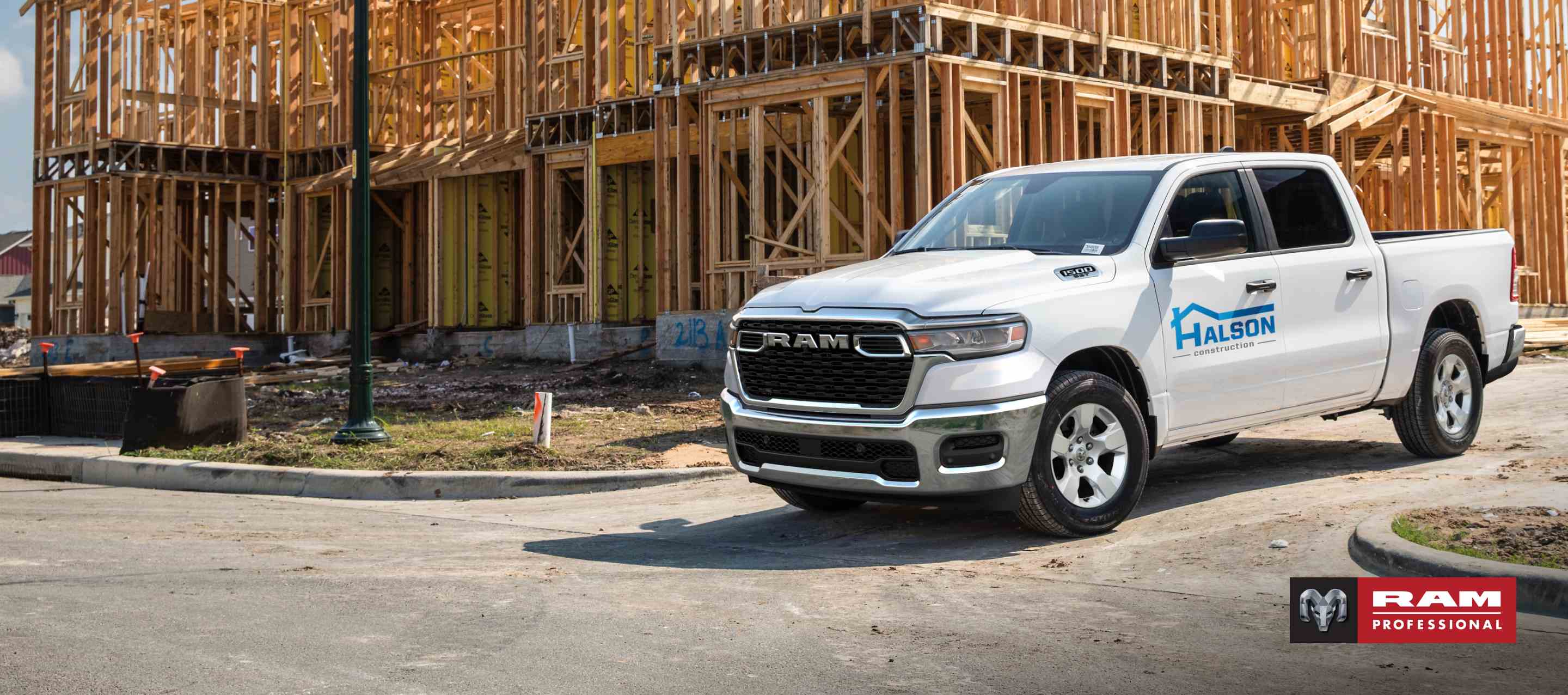 Una Ram 1500 Tradesman 4x4 Crew Cab 2025 blanca con el rótulo de una empresa de construcción en la puerta del conductor, estacionada en una obra. Ram Professional.