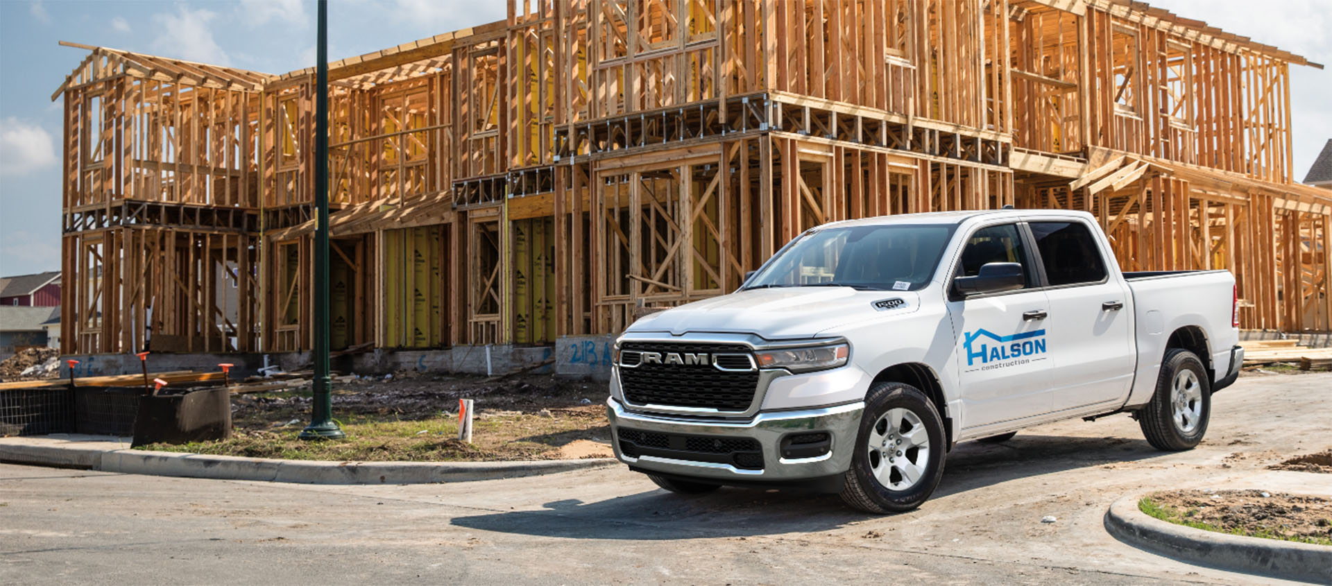 Una Ram 1500 Tradesman 4x4 Crew Cab 2025 blanca con el rótulo de una empresa de construcción en la puerta del conductor, estacionada en una obra.