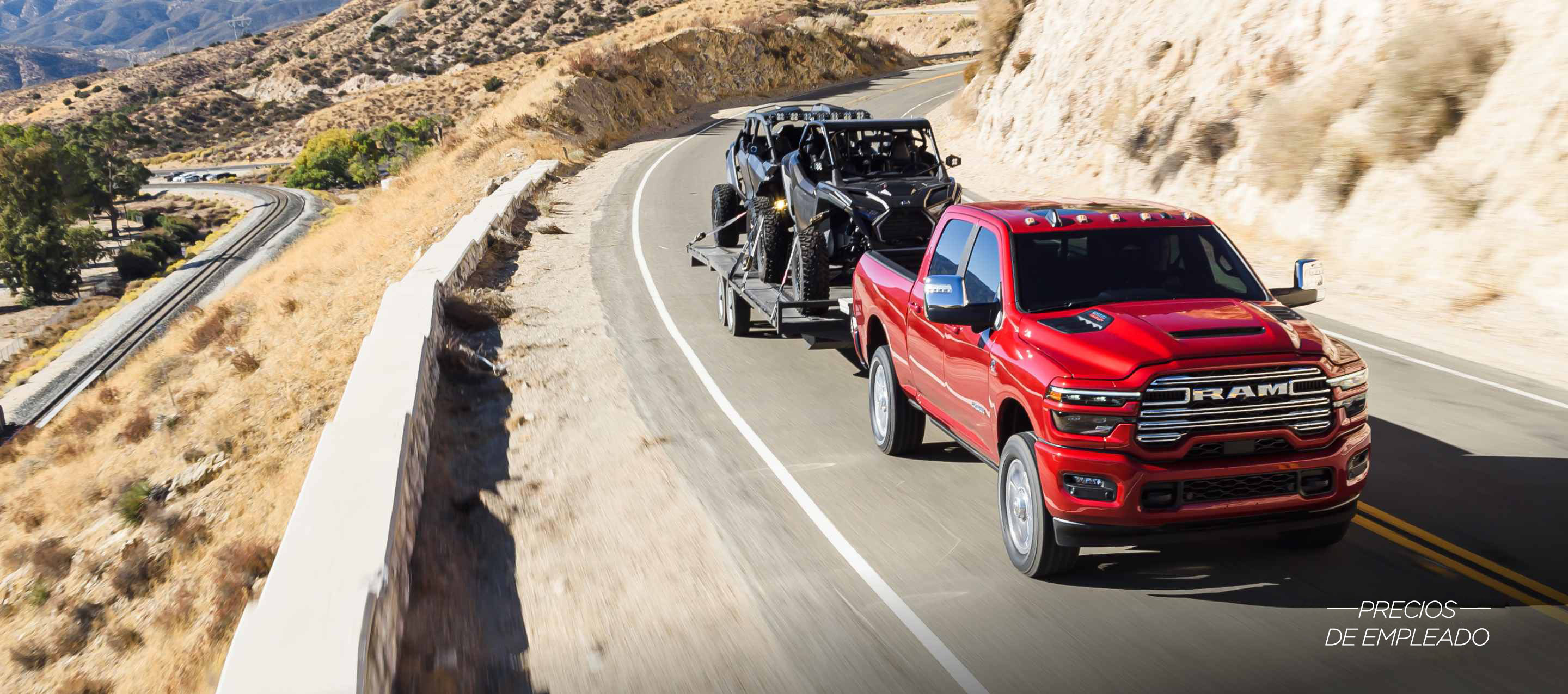 Una Ram 2500 Laramie 4x4 Crew Cab 2025 roja circulando por una carretera en las montañas, mientras remolca dos ATV. Evento de ventas Precios de empleado.