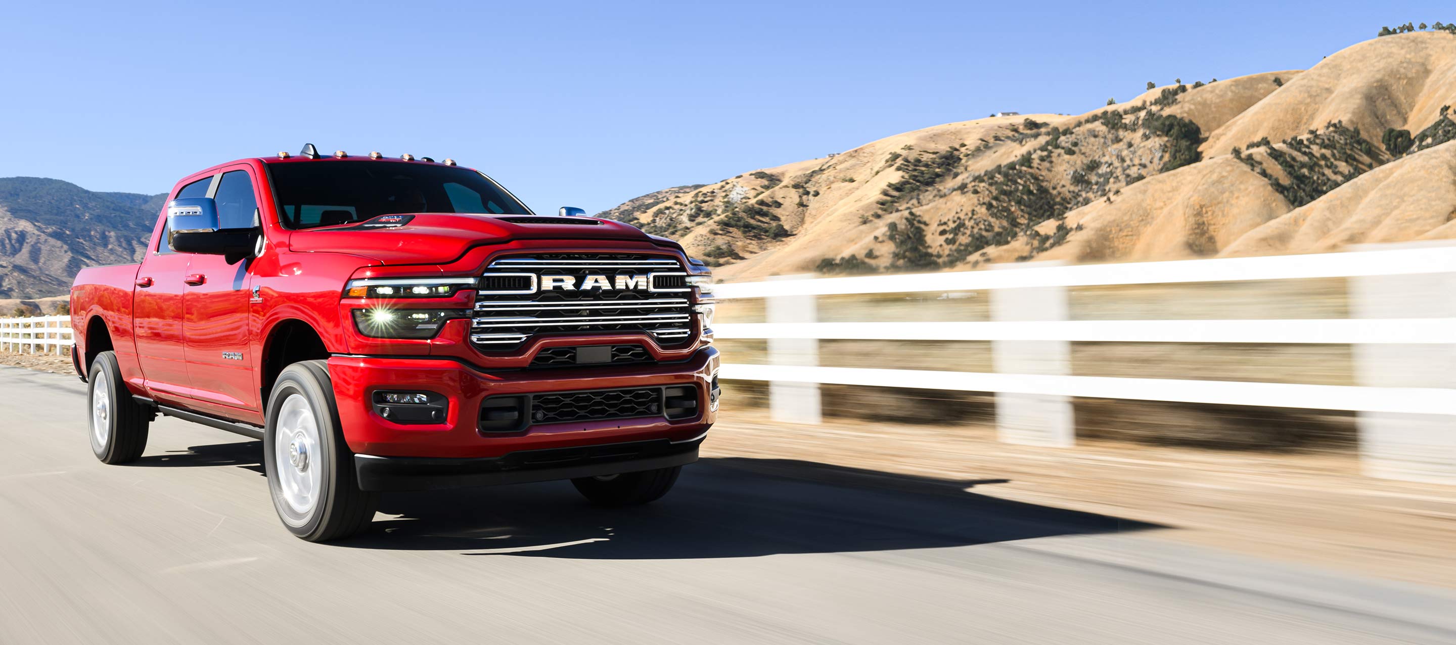 Una Ram 2500 Laramie 4x4 Crew Cab 2025 roja circulando por una carretera, con montañas de fondo.