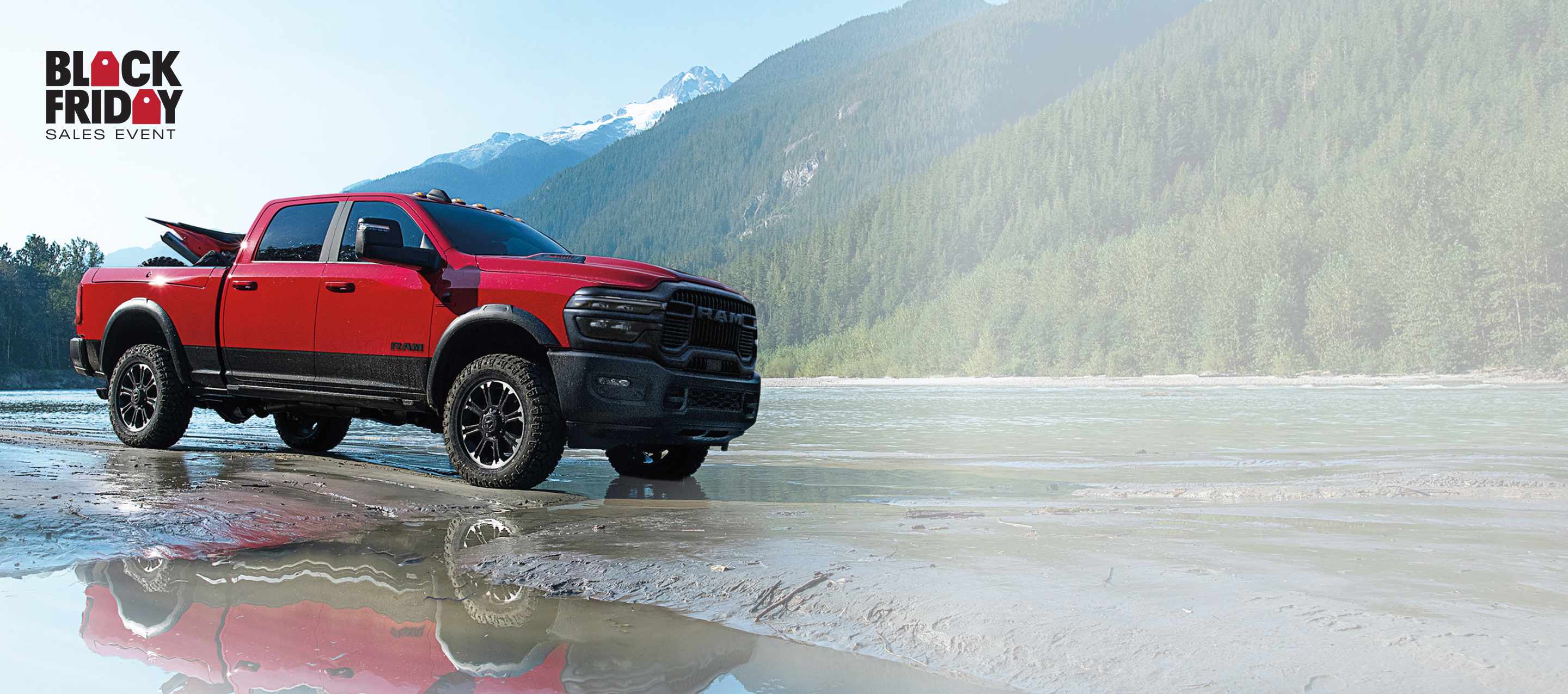 Una Ram 2500 Tradesman 4x4 Crew Cab 2025 blanca acarreando una pala mecánica sobre un remolque de plataforma plana por un sitio de construcción lodoso. Evento de ventas Black Friday.