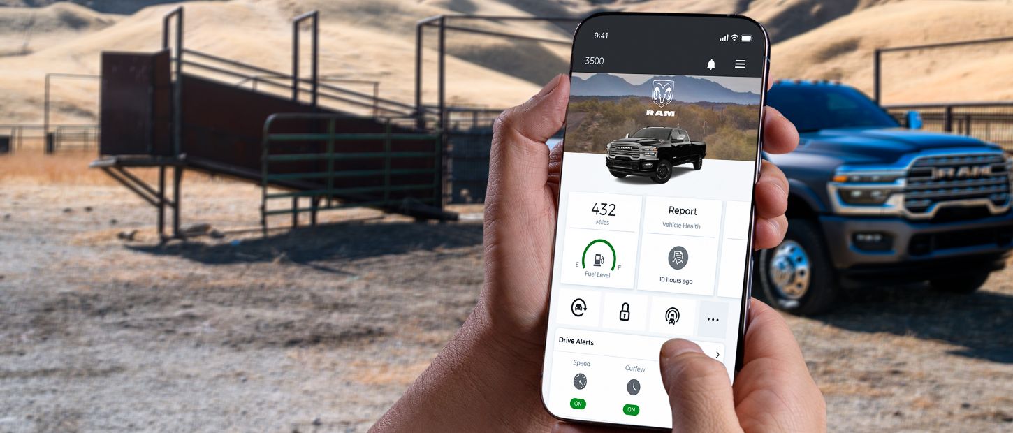 En primer plano, un smartphone exhibe una página de la aplicación Ram; en el fondo, hay una Ram 3500 2025 negra estacionada en un rancho ganadero.