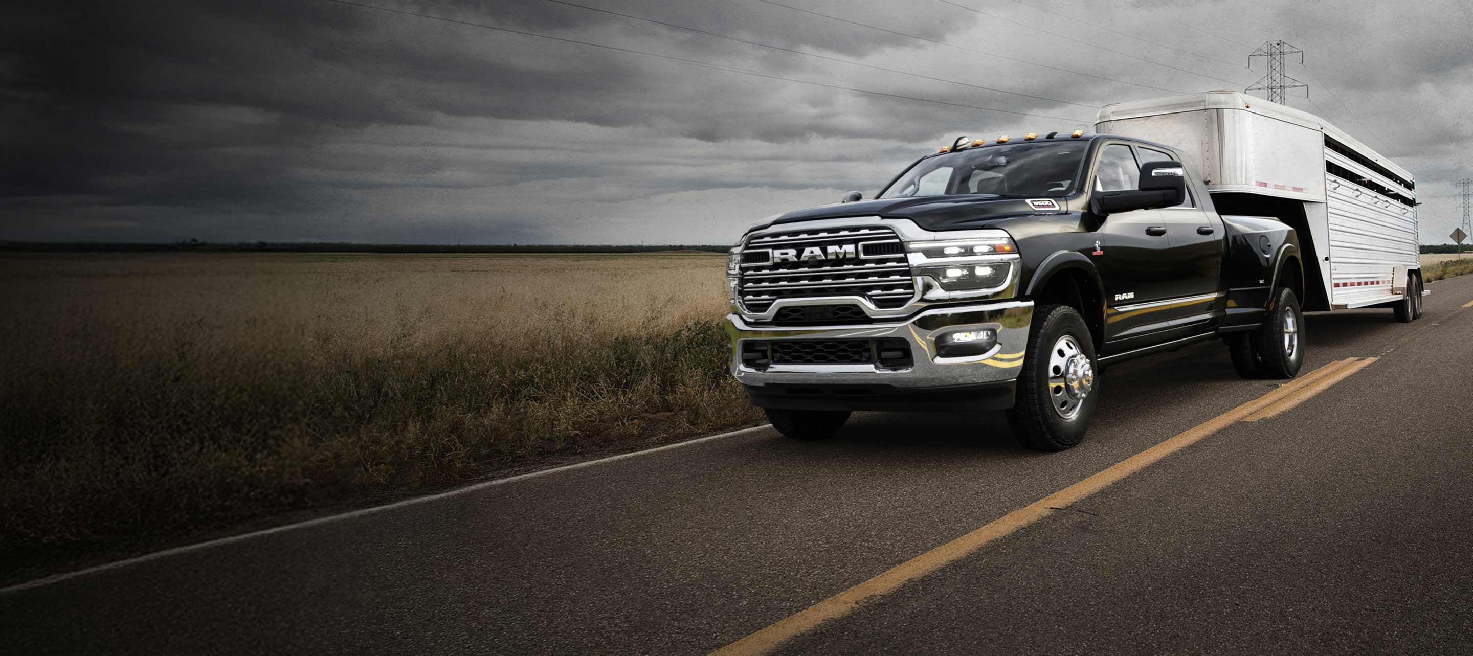 Una Ram 3500 Limited 4x4 Mega Cab 2025 negra circula por una carretera, acarreando un remolque de viaje grande, con nubes de tormenta en lo alto.