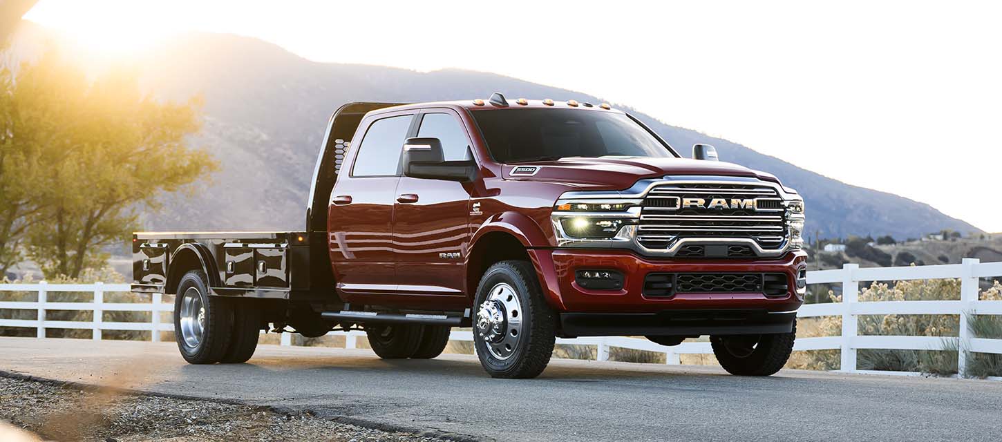 Una Ram 5500 Laramie Chassis Cab Crew Cab 2025 roja con una mejora de plataforma, cirulando por un camino campestre.