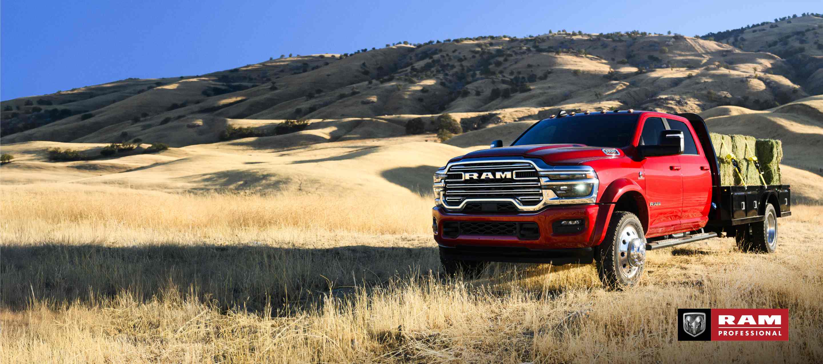 Una Ram 5500 Laramie Chassis Crew Cab 2025 roja transportando varios fardos de heno grandes sobre una mejora de plataforma larga. Ram Professional.