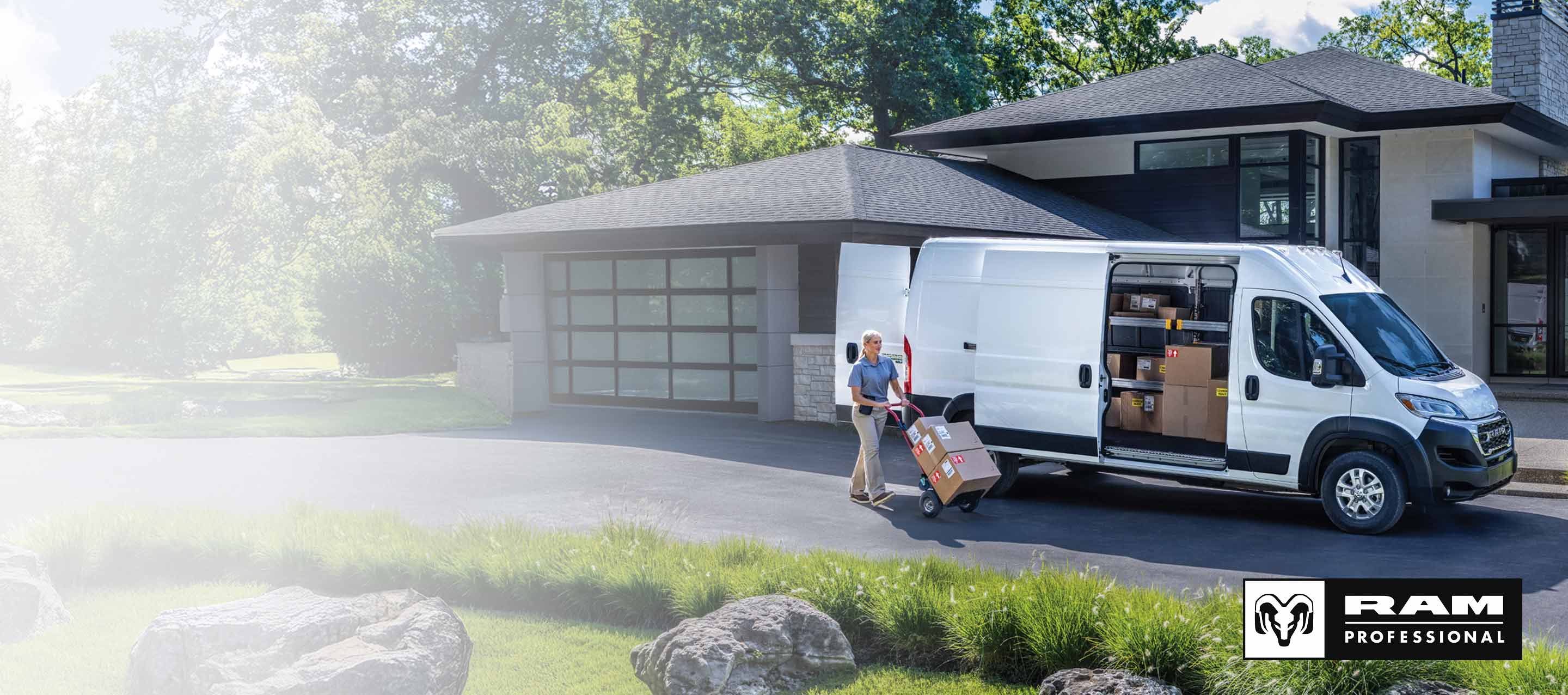 Una Cargo Van Ram ProMaster EV 3500 2026 SLT High Roof blanca con la puerta deslizable del lado del pasajero y las puertas traseras abiertas que permiten ver paquetes en el interior, estacionada en la entrada de una casa del vecindario, con un repartidor cerca empujando una carretilla llena de cajas. Ram Professional.