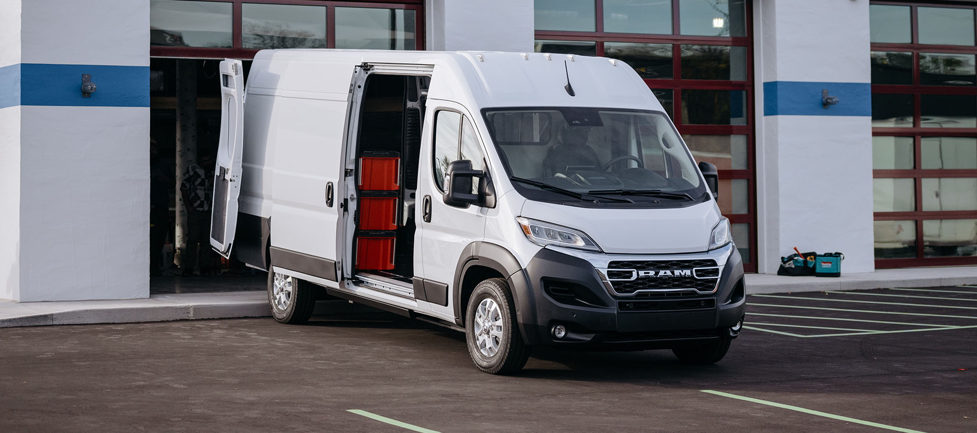 Una Cargo Van Ram ProMaster EV 3500 2025 SLT High Roof blanca con la puerta deslizable del lado del pasajero y las puertas traseras abiertas que permiten observar cajones sobre estantes.