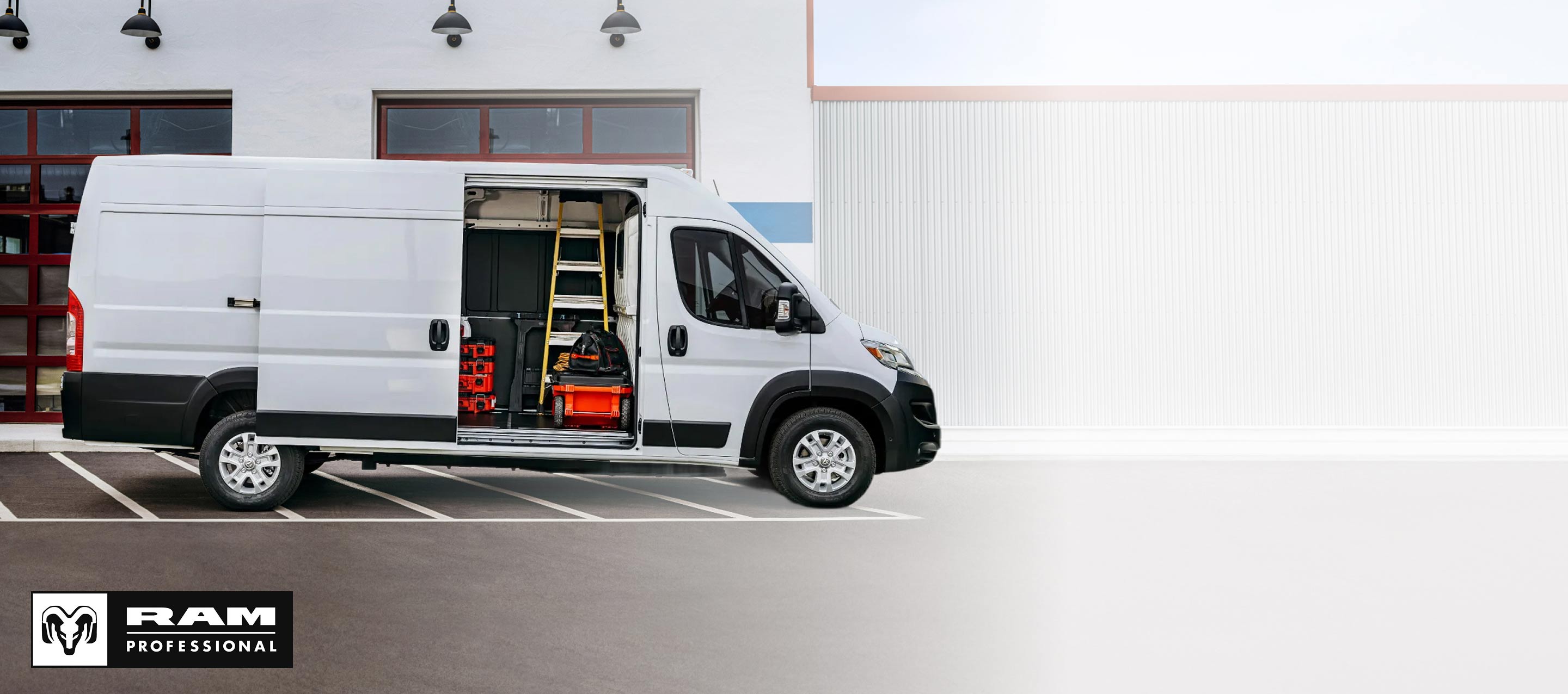 Perfil del lado del pasajero de una Ram ProMaster EV 3500 SLT High Roof Cargo Van 2025 blanca estacionada al lado de un garaje comercial con la puerta lateral corrediza abierta, lo que permite ver herramientas, equipos y una escalera en el interior. Ram Professional.