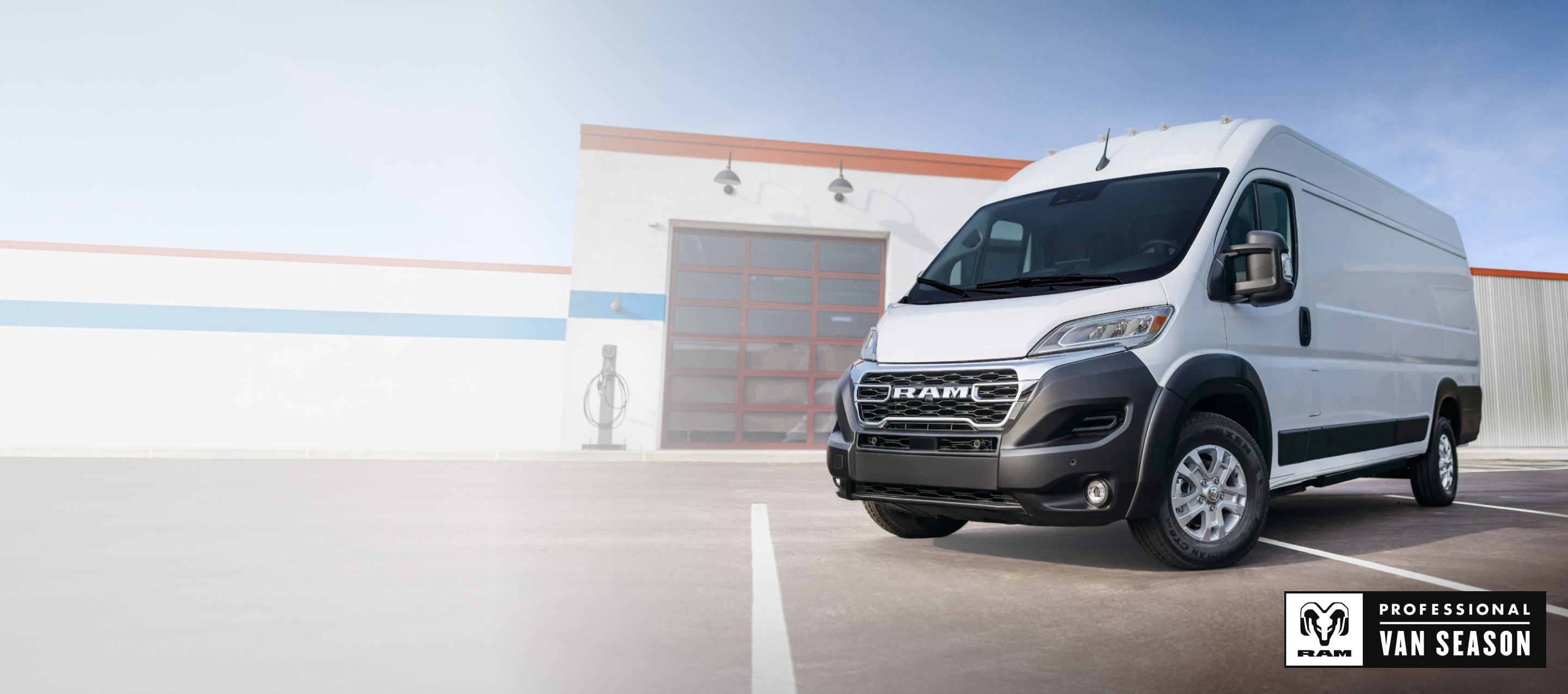 Ángulo delantero del lado del conductor de una Ram ProMaster EV 3500 SLT High Roof Cargo Van 2025 blanca estacionada cerca de un garaje comercial. Temporada de vans profesionales Ram.