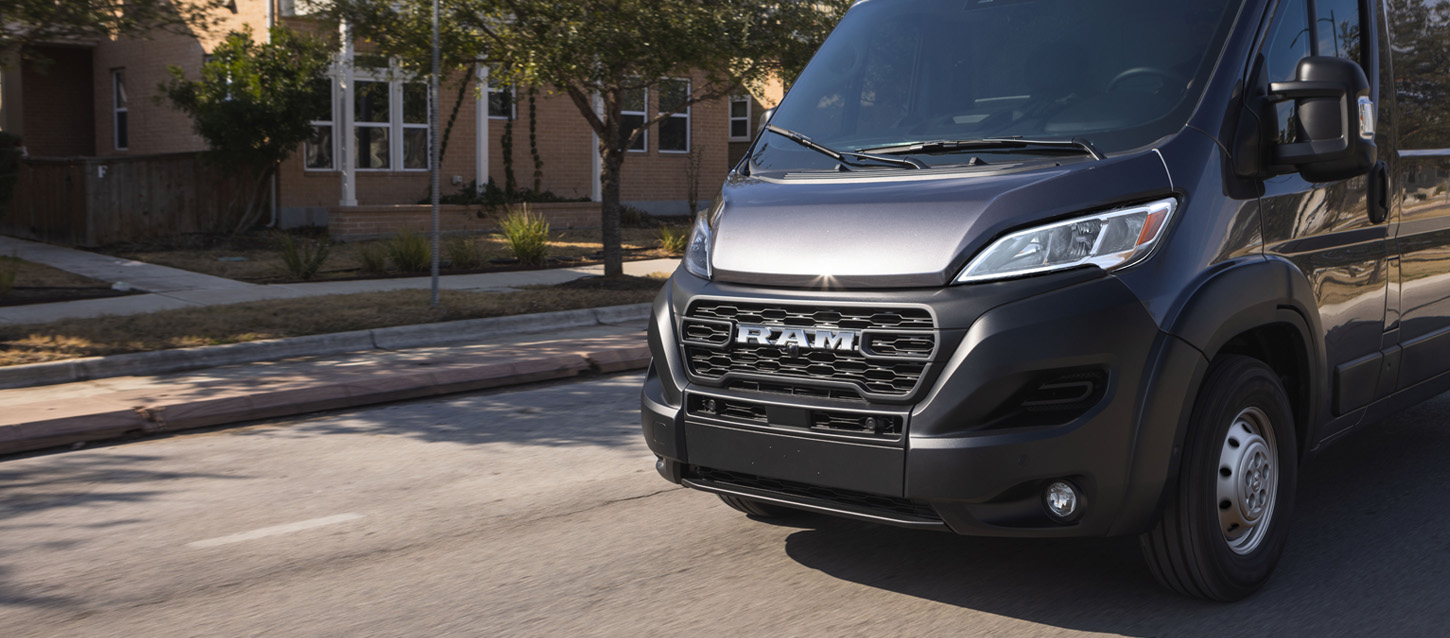 Una Ram ProMaster 2500 Tradesman Cargo Van High Roof 2025 negra circulando por un barrio residencial.