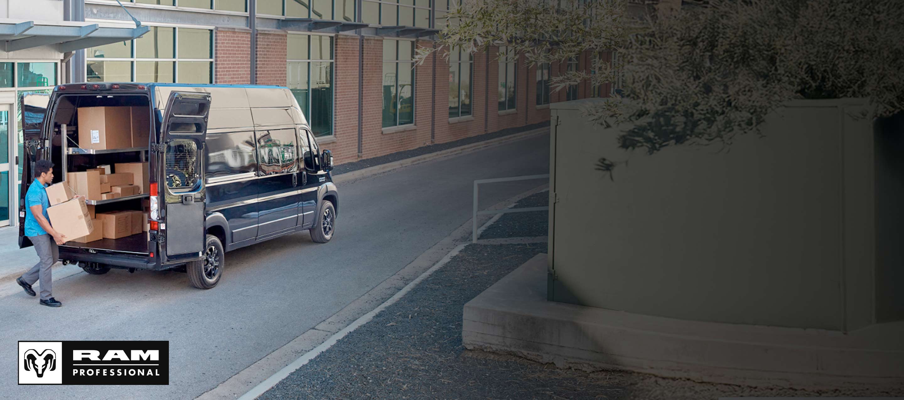 Un hombre lleva paquetes hacia las puertas traseras abiertas de una Ram ProMaster 3500 SLT Plus Super High Roof Cargo Van 2025 negra con el área de carga llena de cajas. Ram Professional.