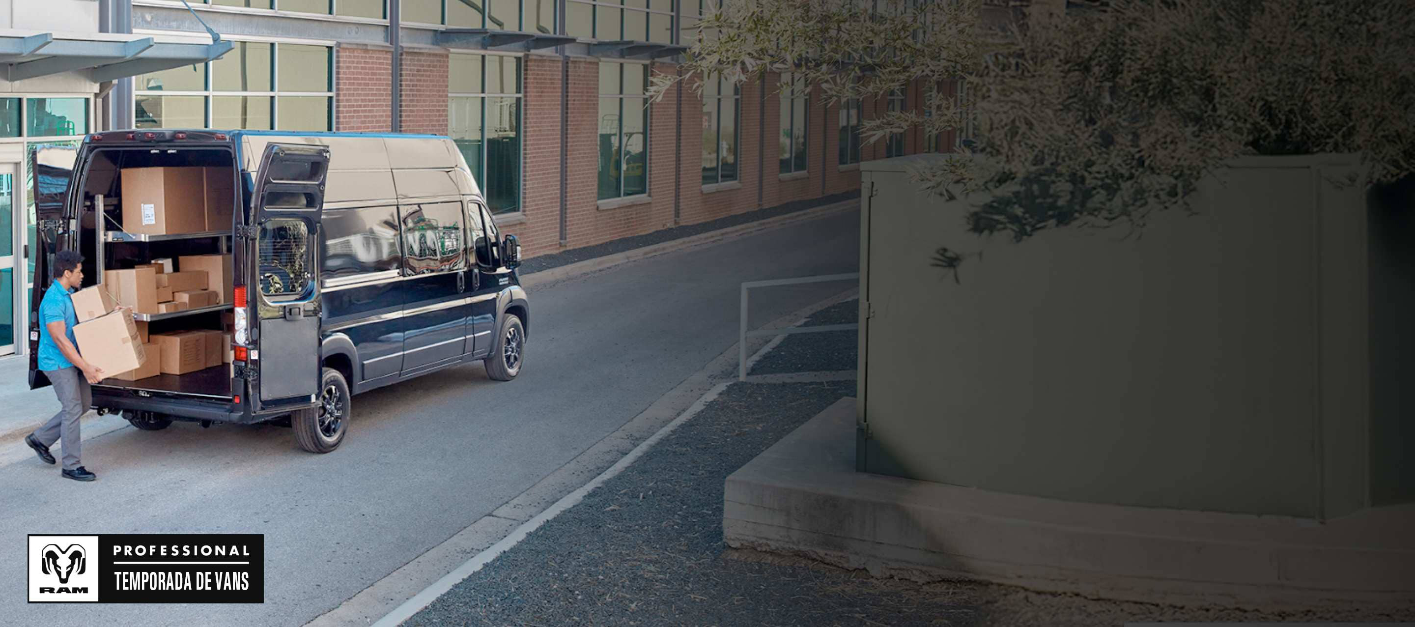 Un hombre lleva paquetes hacia las puertas traseras abiertas de una Ram ProMaster 3500 SLT Plus Super High Roof Cargo Van 2025 negra con el área de carga llena de cajas. Temporada de vans profesionales Ram.