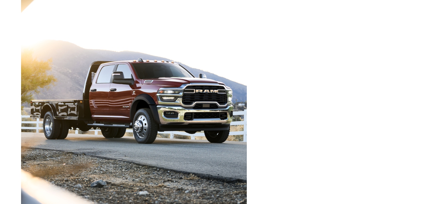 Una Ram 4500 Big Horn Chassis Cab Crew Cab 2026 roja con una mejora de plataforma larga atravesando una carretera con vallas blancas a ambos lados.