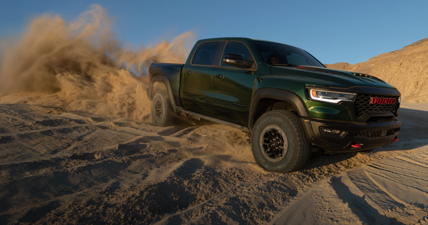 Ángulo delantero del lado del pasajero de una Ram 1500 SRT TRX 4x4 Crew Cab 2026 verde circulando por el desierto, fuera de la carretera, levantando una nube de arena a su paso.
