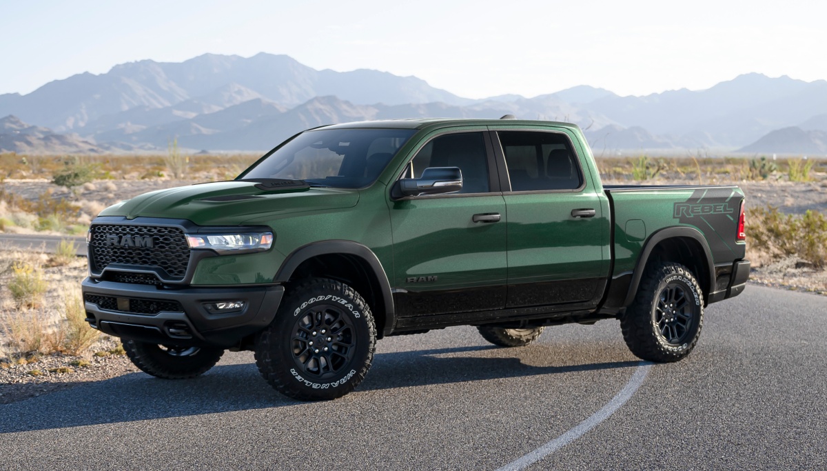 Se muestra una Ram 1500 Rebel 4x4 Crew Cab 2026 verde estacionada en un camino desértico, con montañas de fondo.