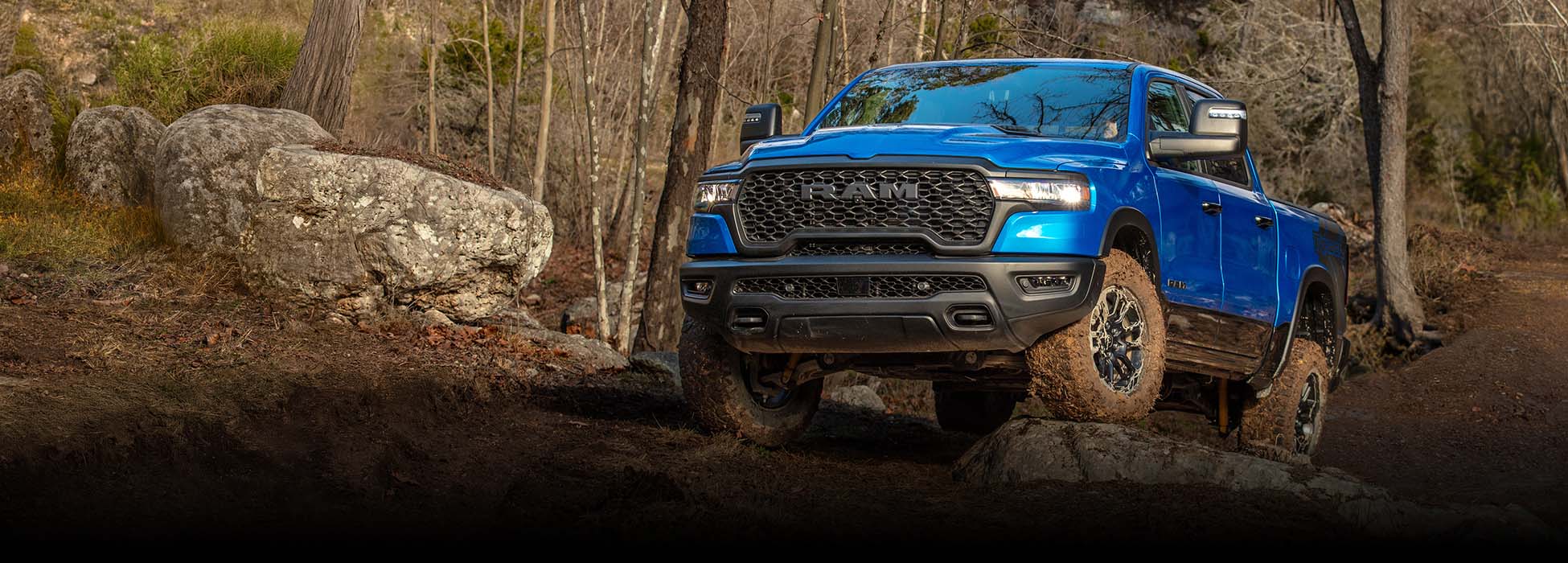 Una Ram 1500 Rebel 4x4 Crew Cab 2026 trepando por un terreno rocoso todoterreno con un bosque de fondo.