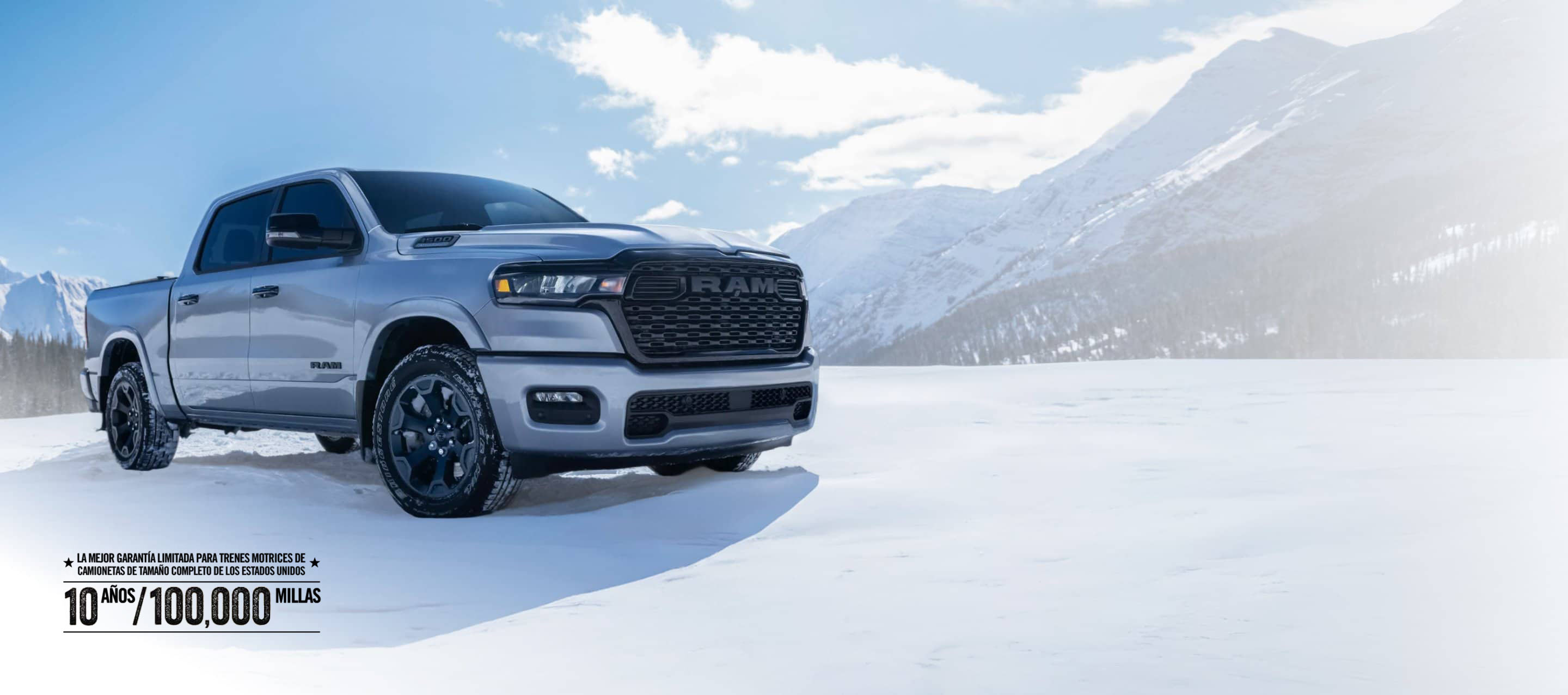 A white 2026 Ram 1500 Big Horn 4x4 Crew Cab parked on a snow-covered clearing off-road in the mountains. Limited warranty 10yr/ 100,000mi.