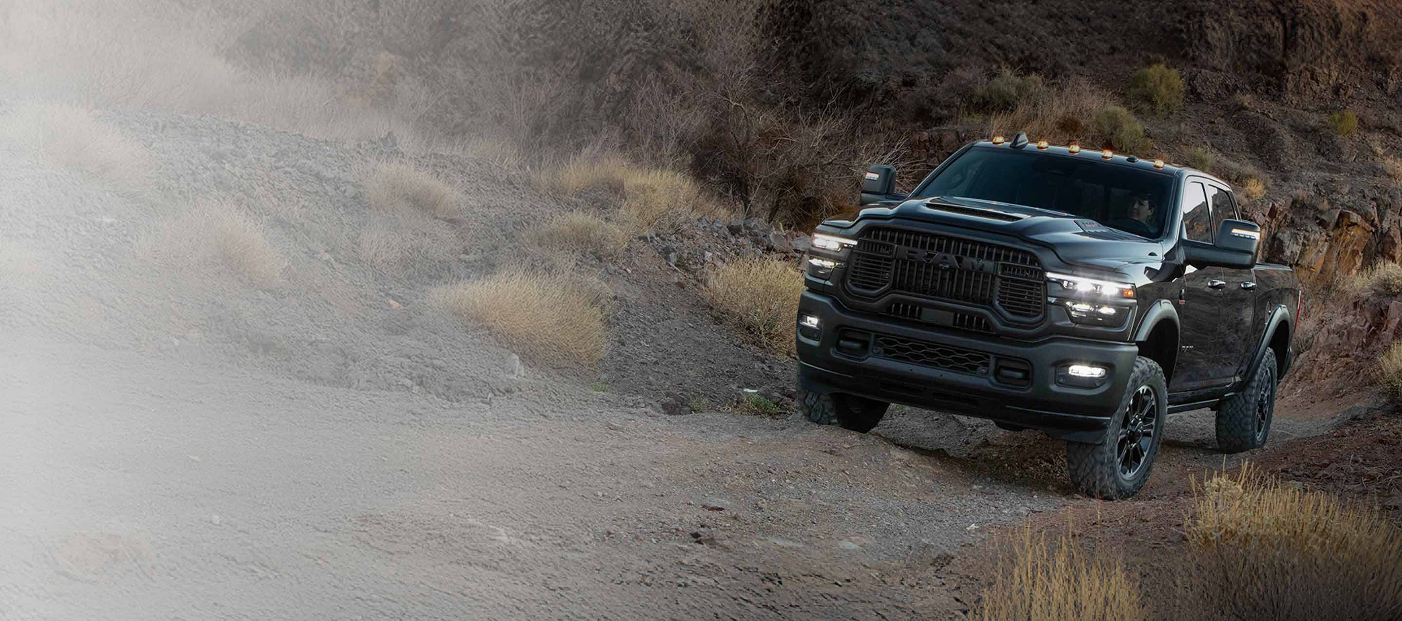 Una Ram 1500 Limited 4x4 Crew Cab 2026 gris circulando por un camino campestre. Evento de ventas Drive Into Fall y 10 AÑOS/100000 millas.