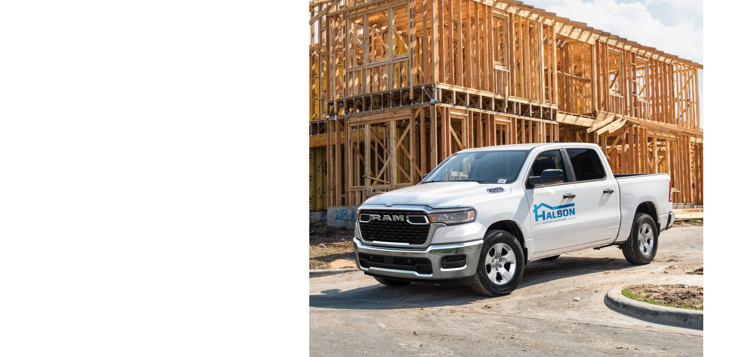 Una Ram 1500 Tradesman 4x4 Crew Cab 2026 blanca con el rótulo de una empresa de construcción en la puerta del conductor, estacionada en una obra.