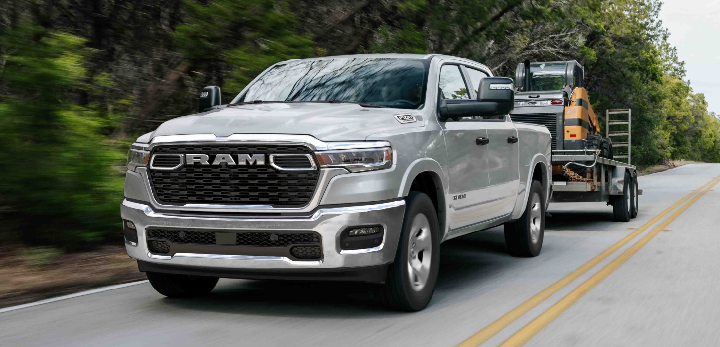 Una Ram 1500 Big Horn 4x4 Crew Cab 2026 plateada remolcando equipos motorizados mientras viaja por una carretera.